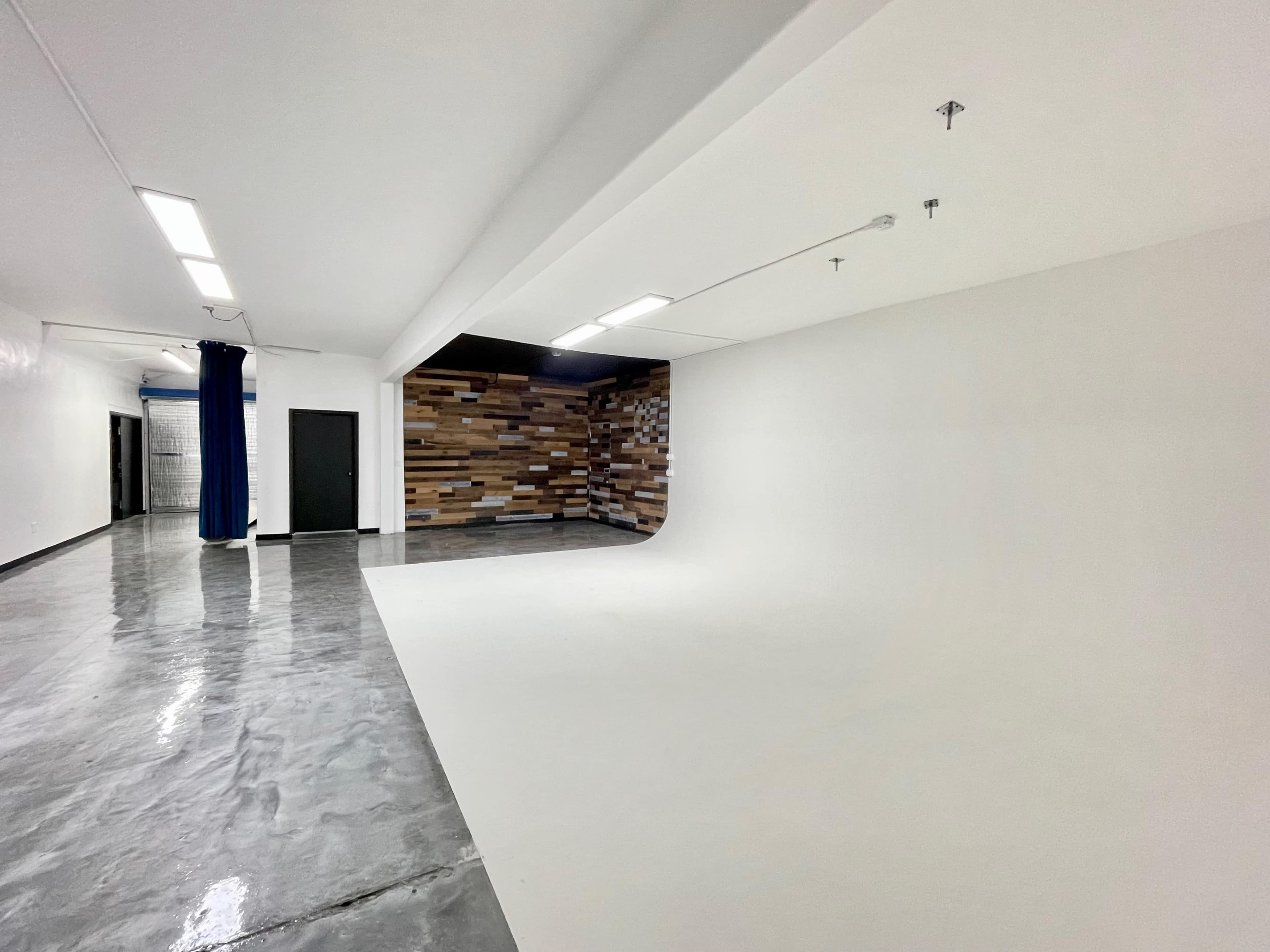 An empty room with a white backdrop and a textured wooden wall, featuring polished concrete flooring.