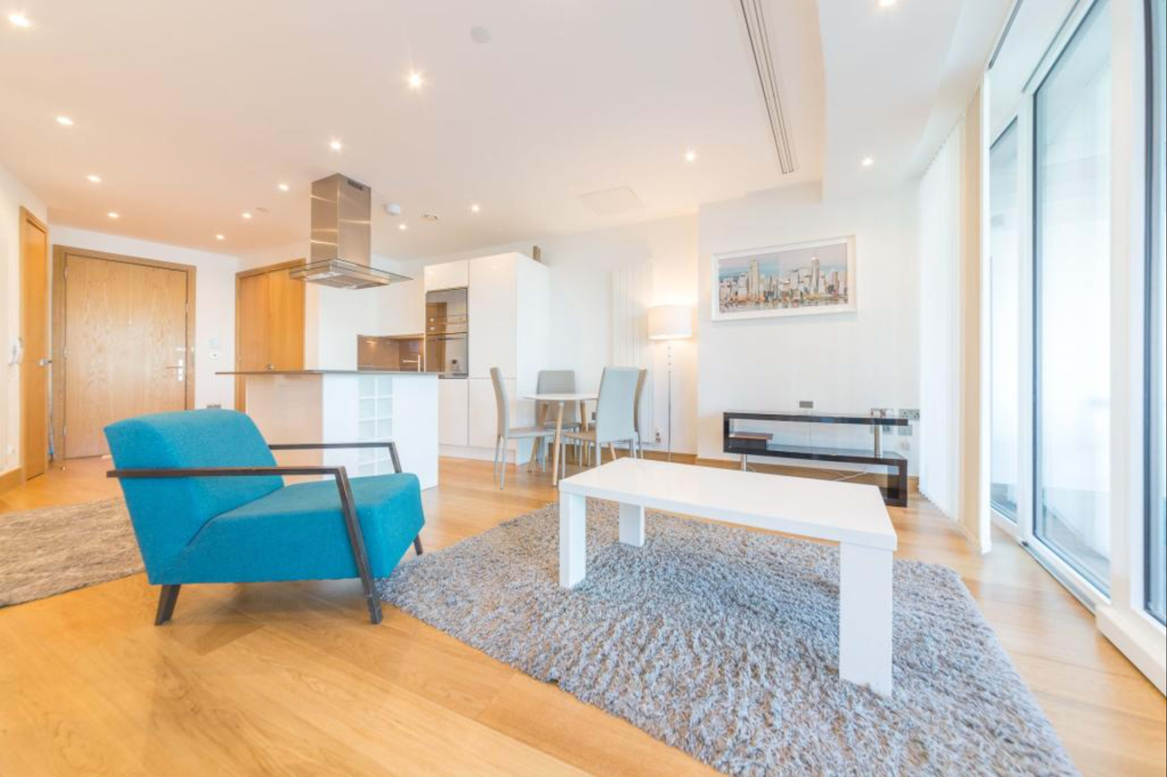 The image shows a modern living space with a blue armchair, a white coffee table, and a dining area in an open floor plan.