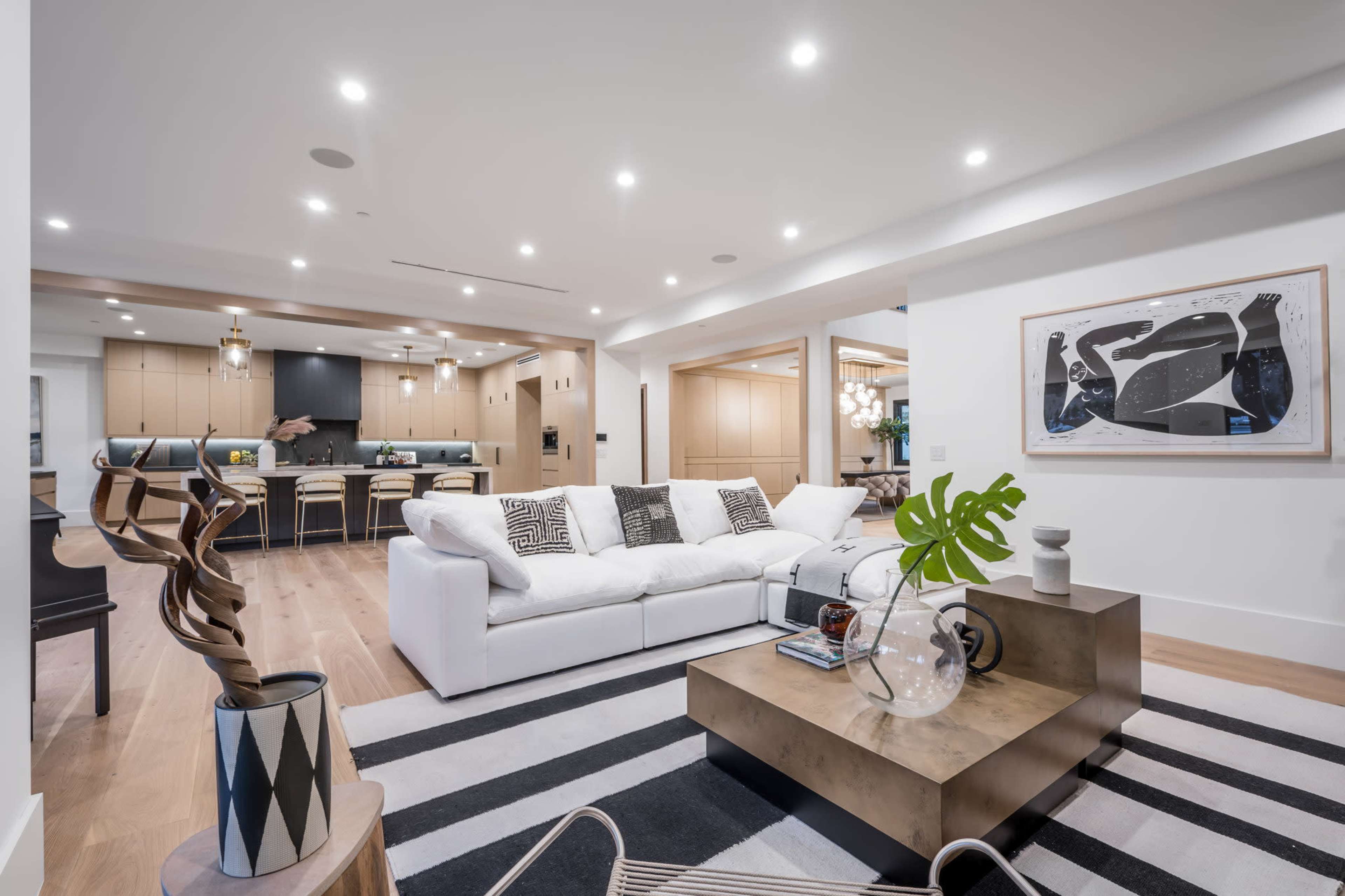 A modern living room featuring a white sofa, a striped area rug, and a coffee table with decorative items, leading into a kitchen with wood cabinetry in the background.
