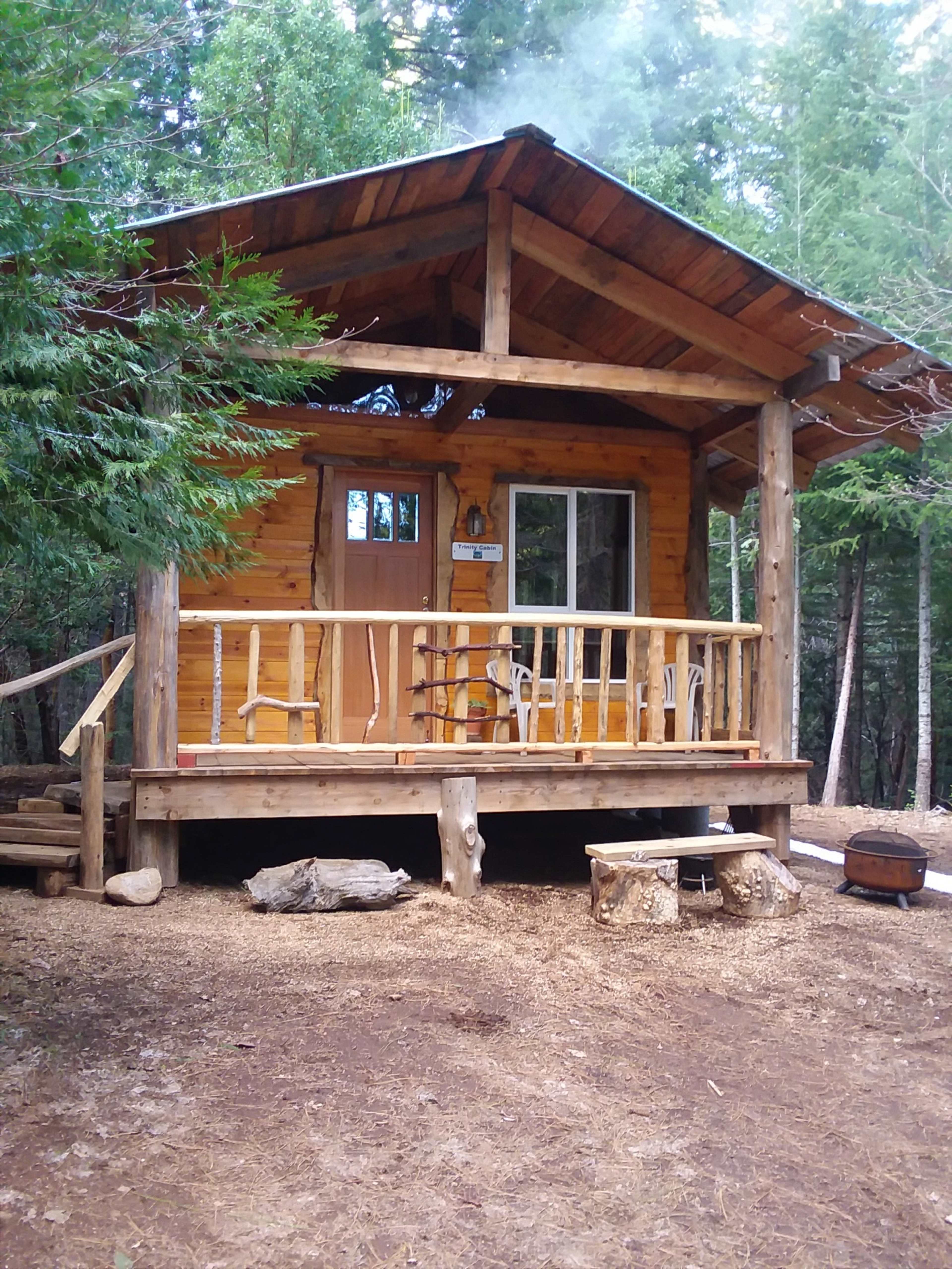 A wooden cabin with a porch sits among trees in a forested area.