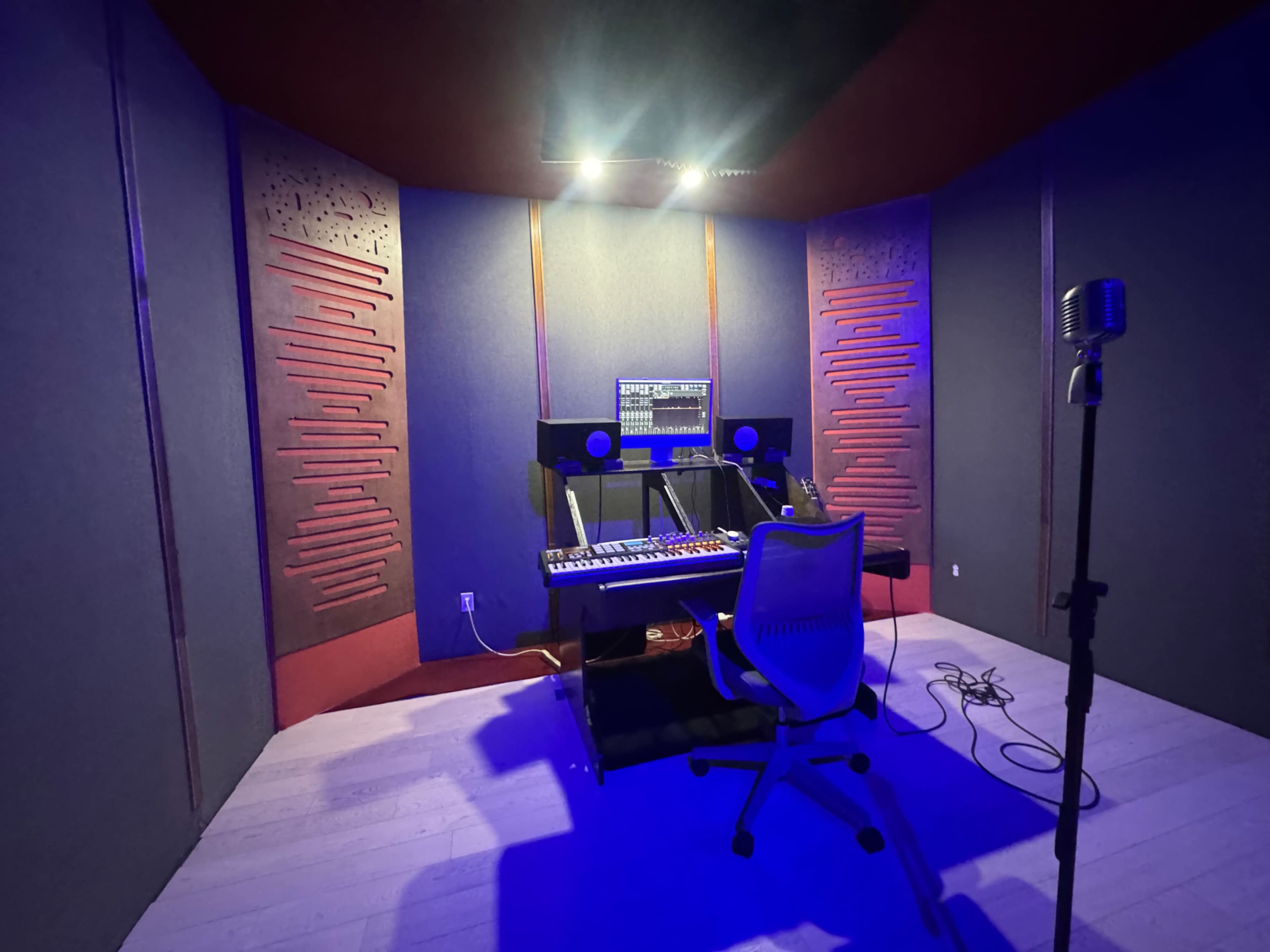 The image shows a dimly lit recording studio featuring a keyboard, computer monitor, and microphone setup.