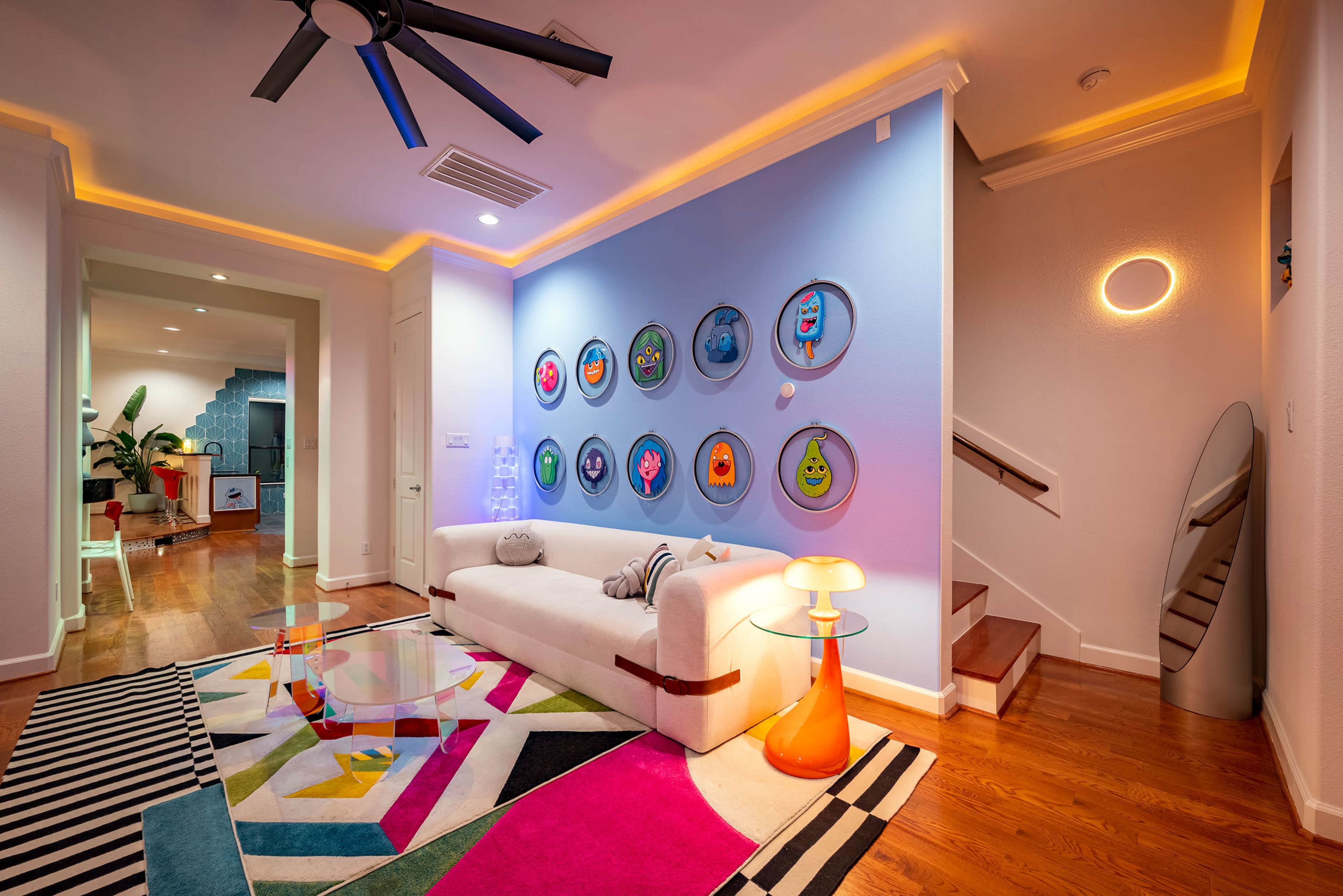The image shows a modern living room with a white sofa, colorful artwork on the wall, and a striped rug.