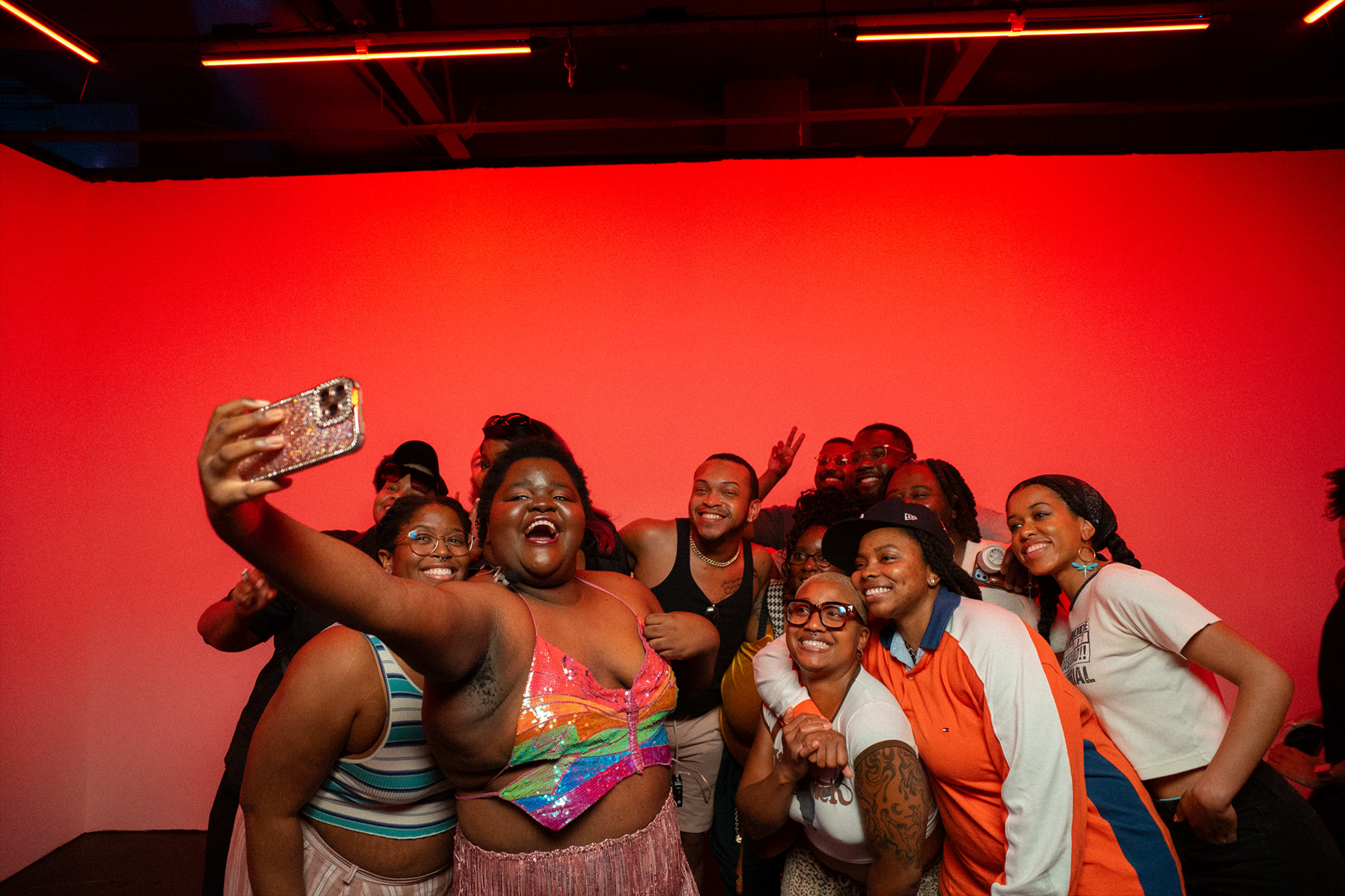 A group of people poses for a selfie in front of a red-lit background.