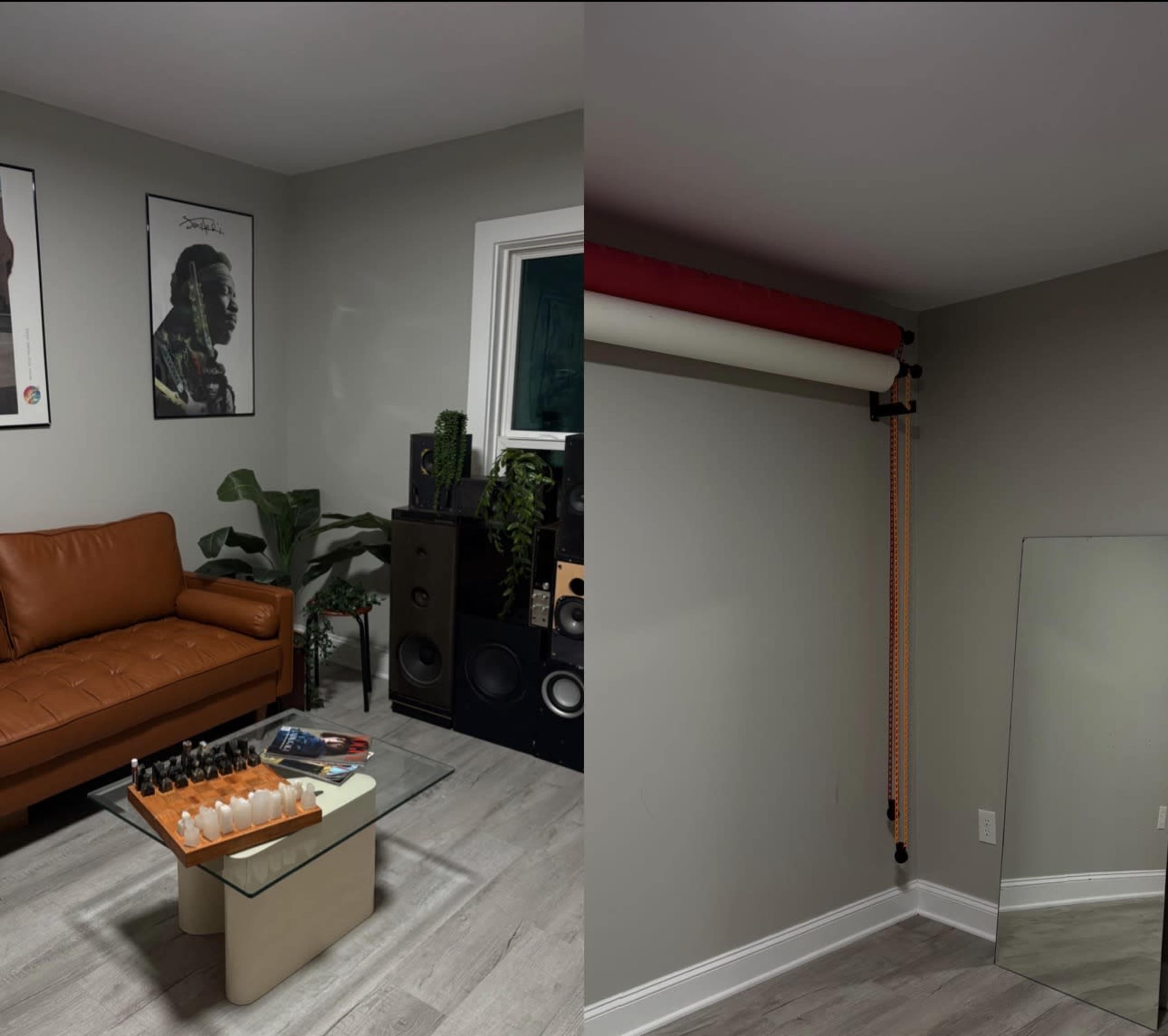 The image shows a room with a brown leather couch, audio speakers, a plant, and a mirror next to a backdrop setup against a gray wall.