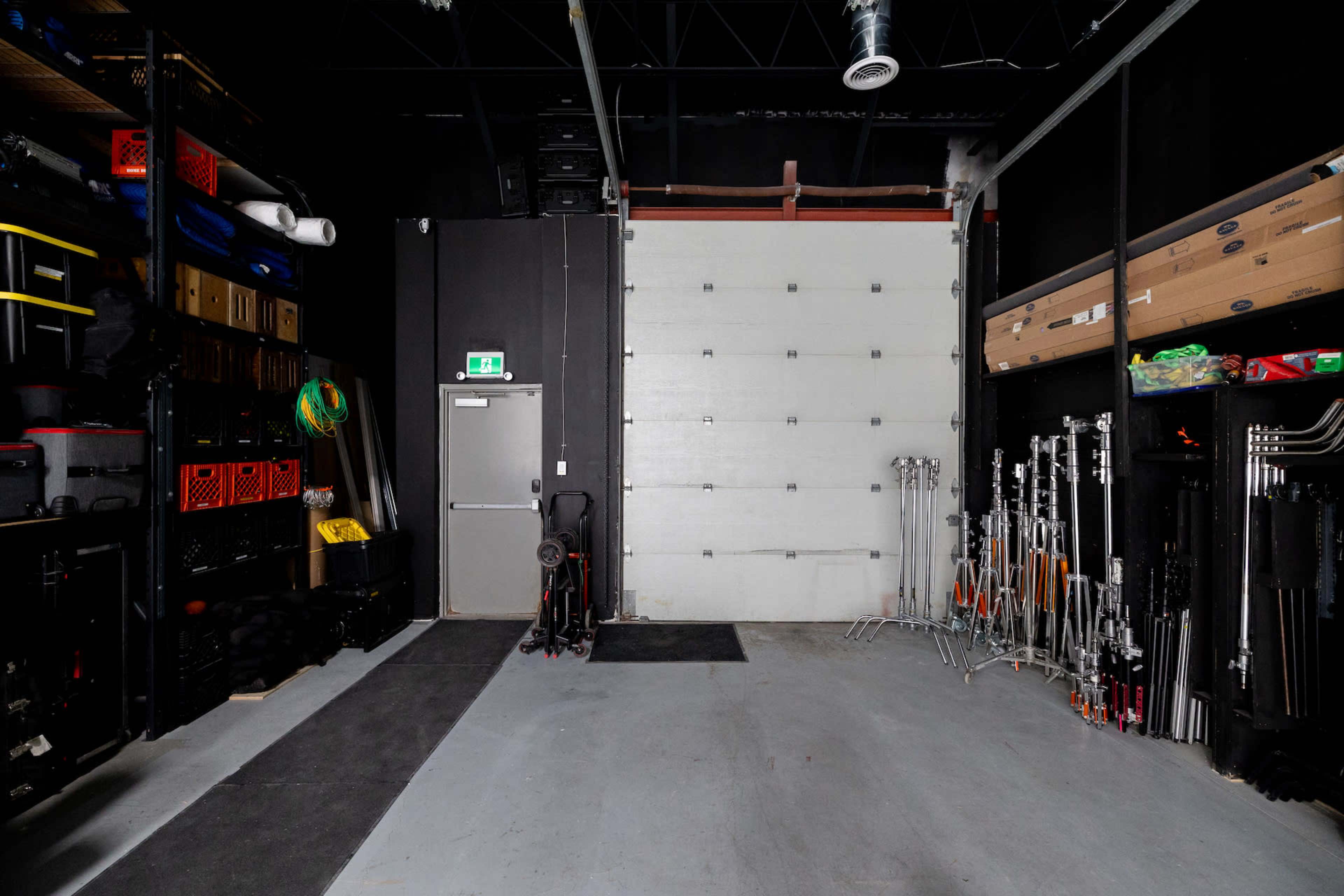 A storage garage with shelves filled with equipment on one side and a large garage door at the back.