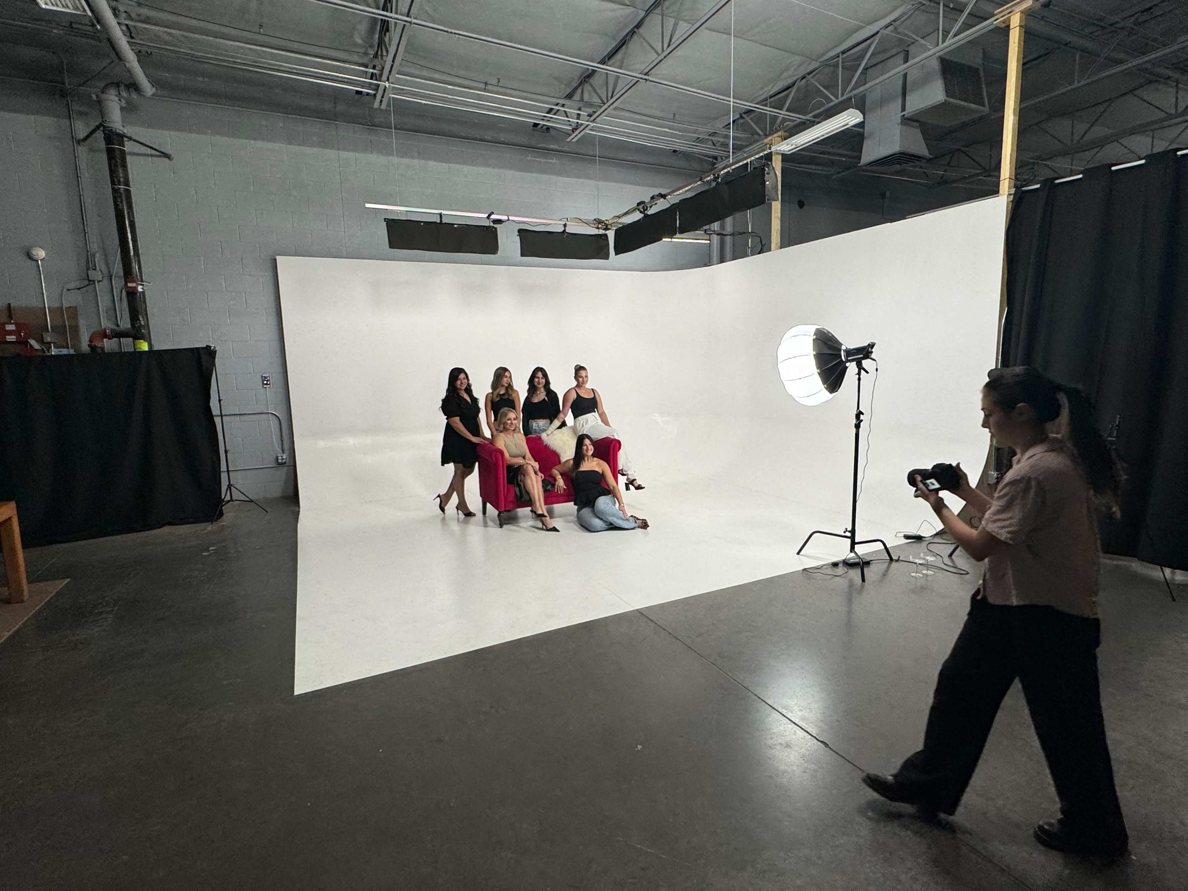 A group of six individuals poses on a white backdrop in a photo studio while a photographer takes their picture.