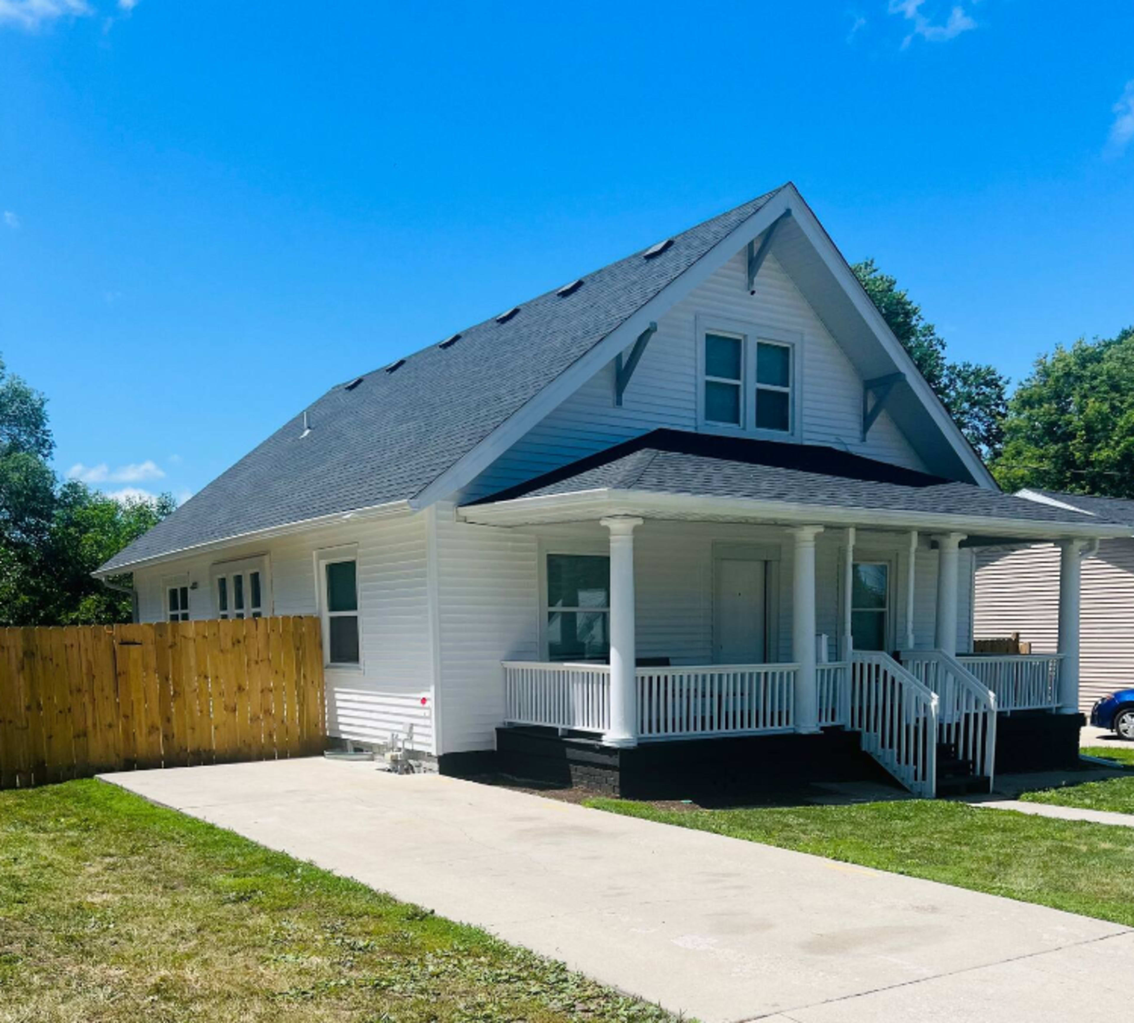 A white, two-story house with a gabled roof, front porch, and a fenced yard.
