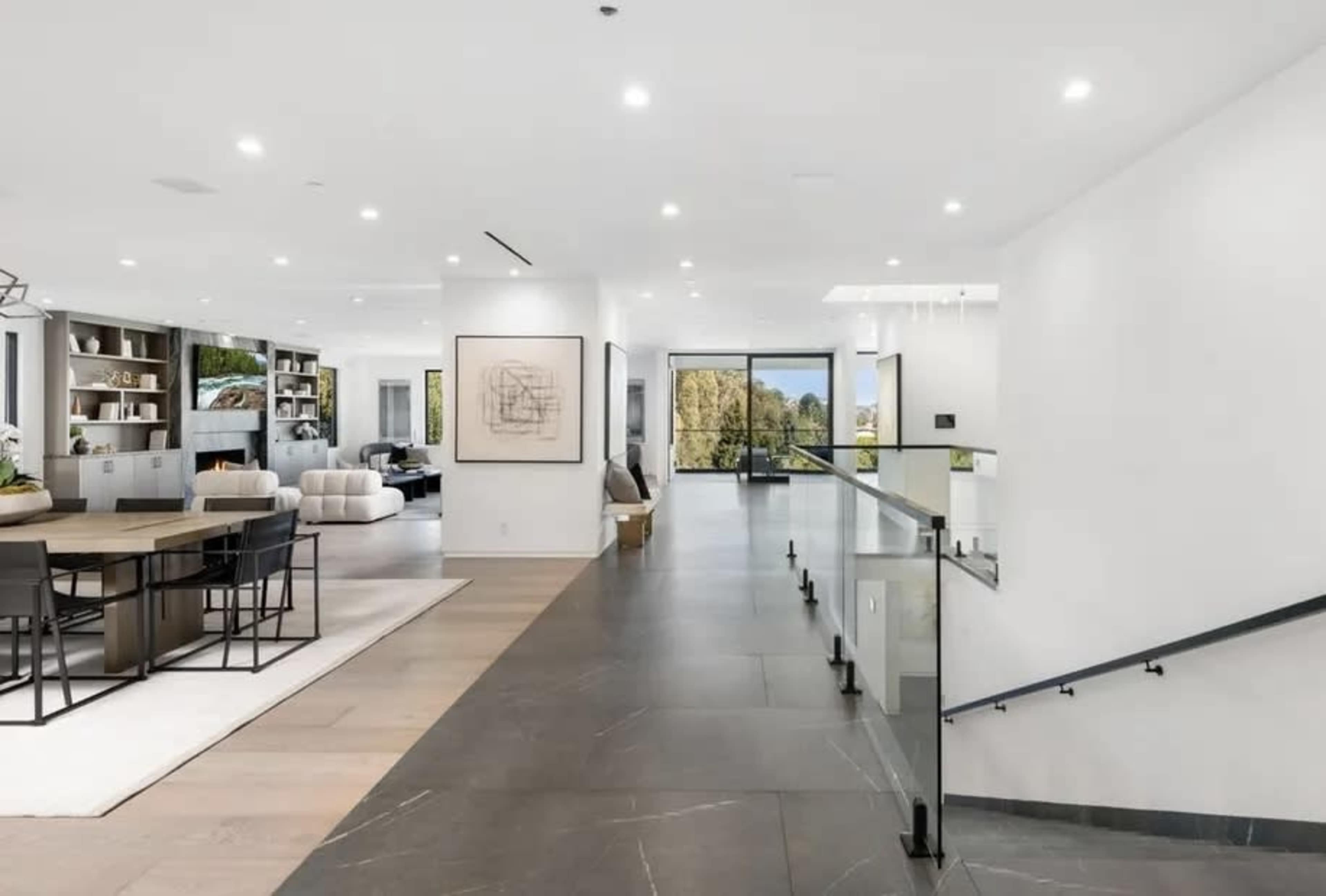 A modern open-concept living space featuring a dining area, a living room, and a staircase with glass railings.