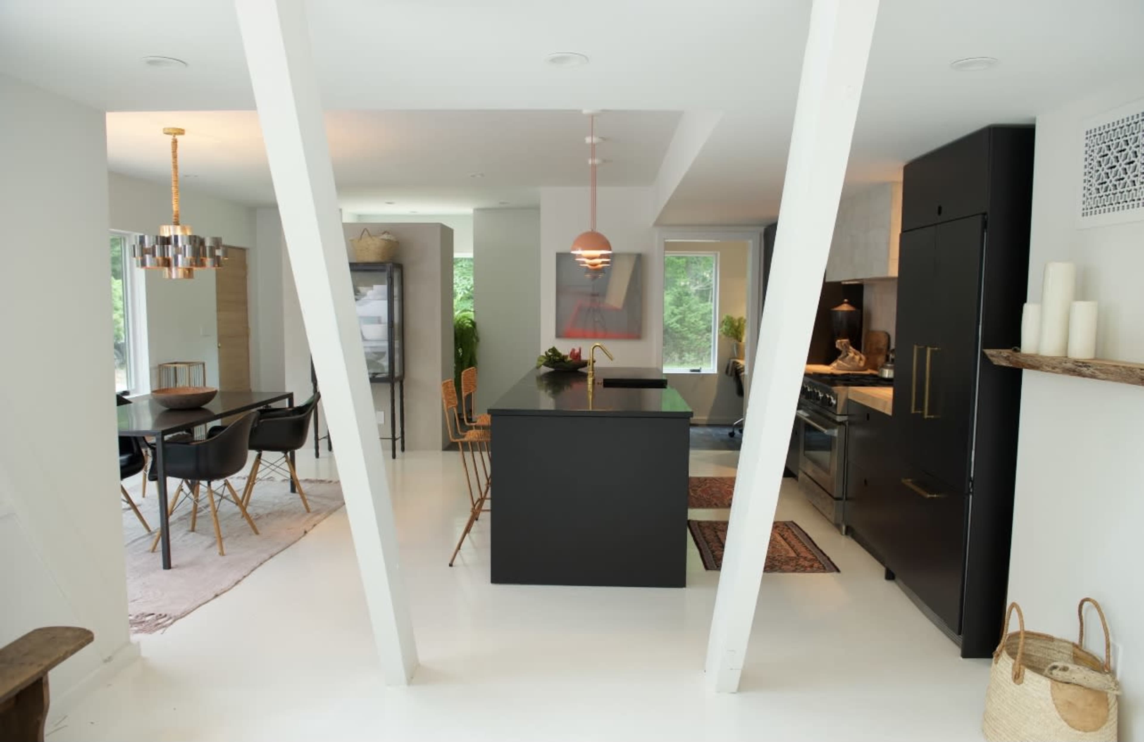 The image shows a modern kitchen and dining area featuring a black kitchen island, wooden dining chairs, and large windows allowing natural light.