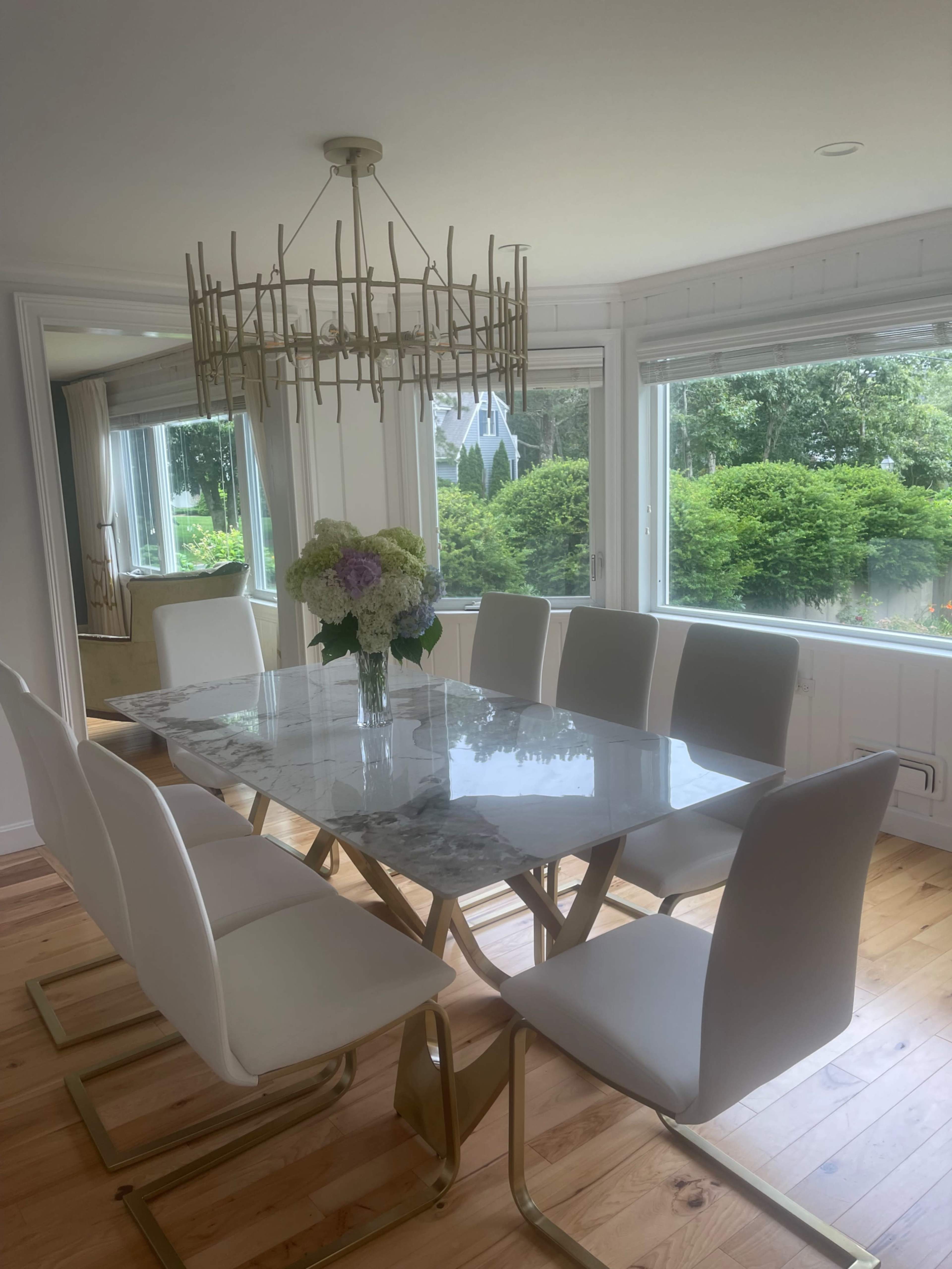 A modern dining room features a marble table with gold accents and white chairs, illuminated by a contemporary chandelier.