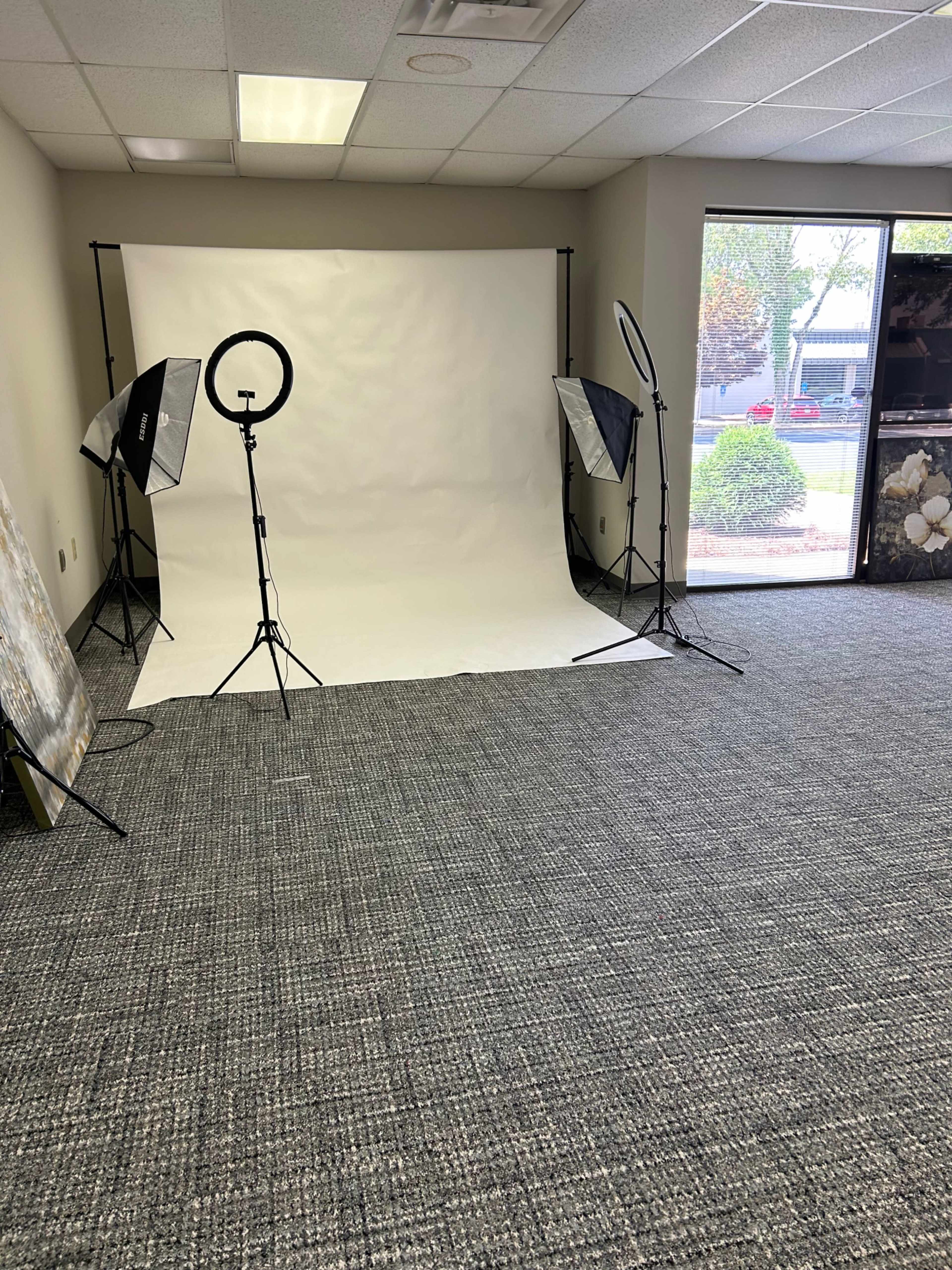 The image shows a photography studio setup with a white backdrop, lighting equipment, and a carpeted floor.
