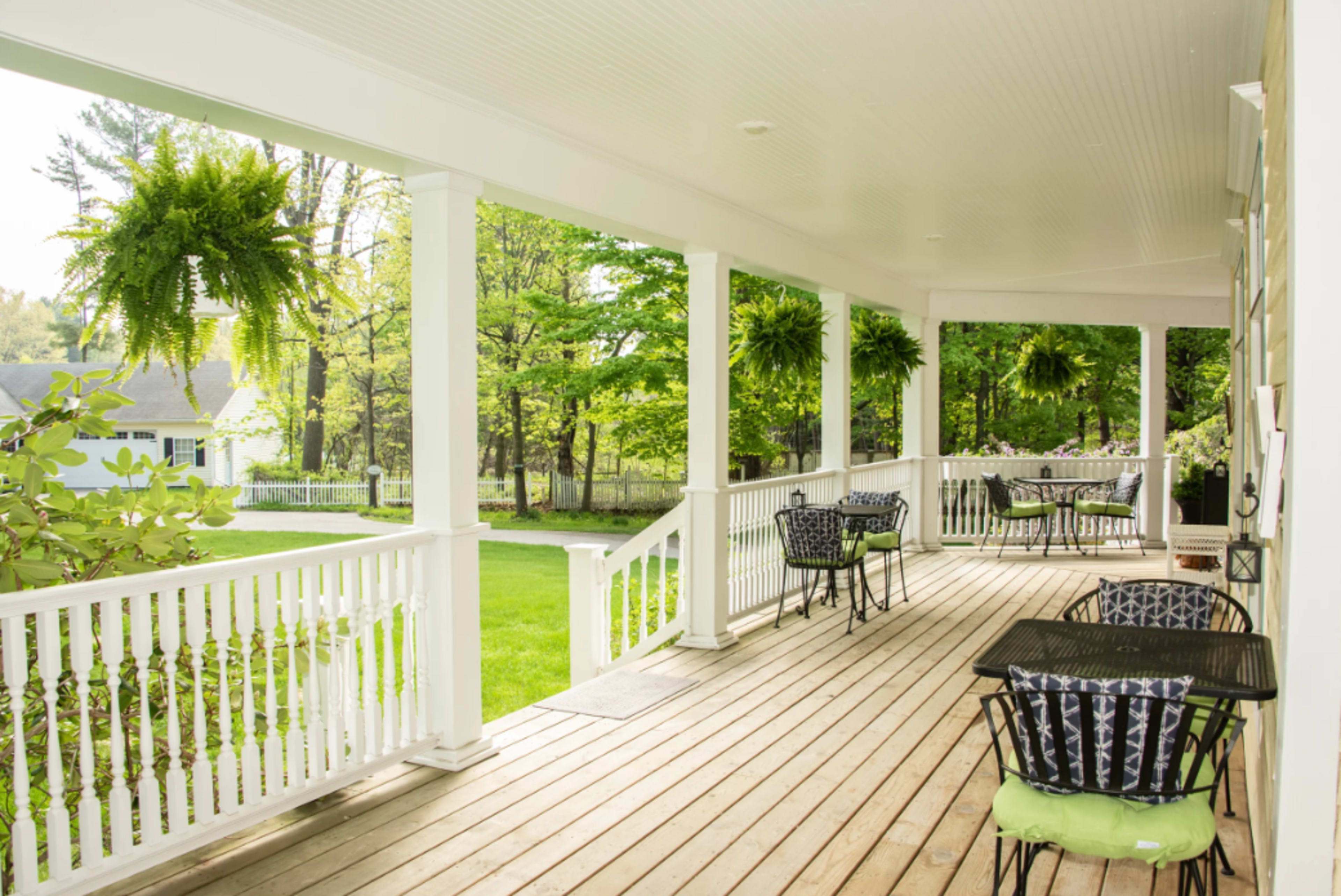 A covered porch with black metal tables and chairs, surrounded by lush greenery and hanging ferns.