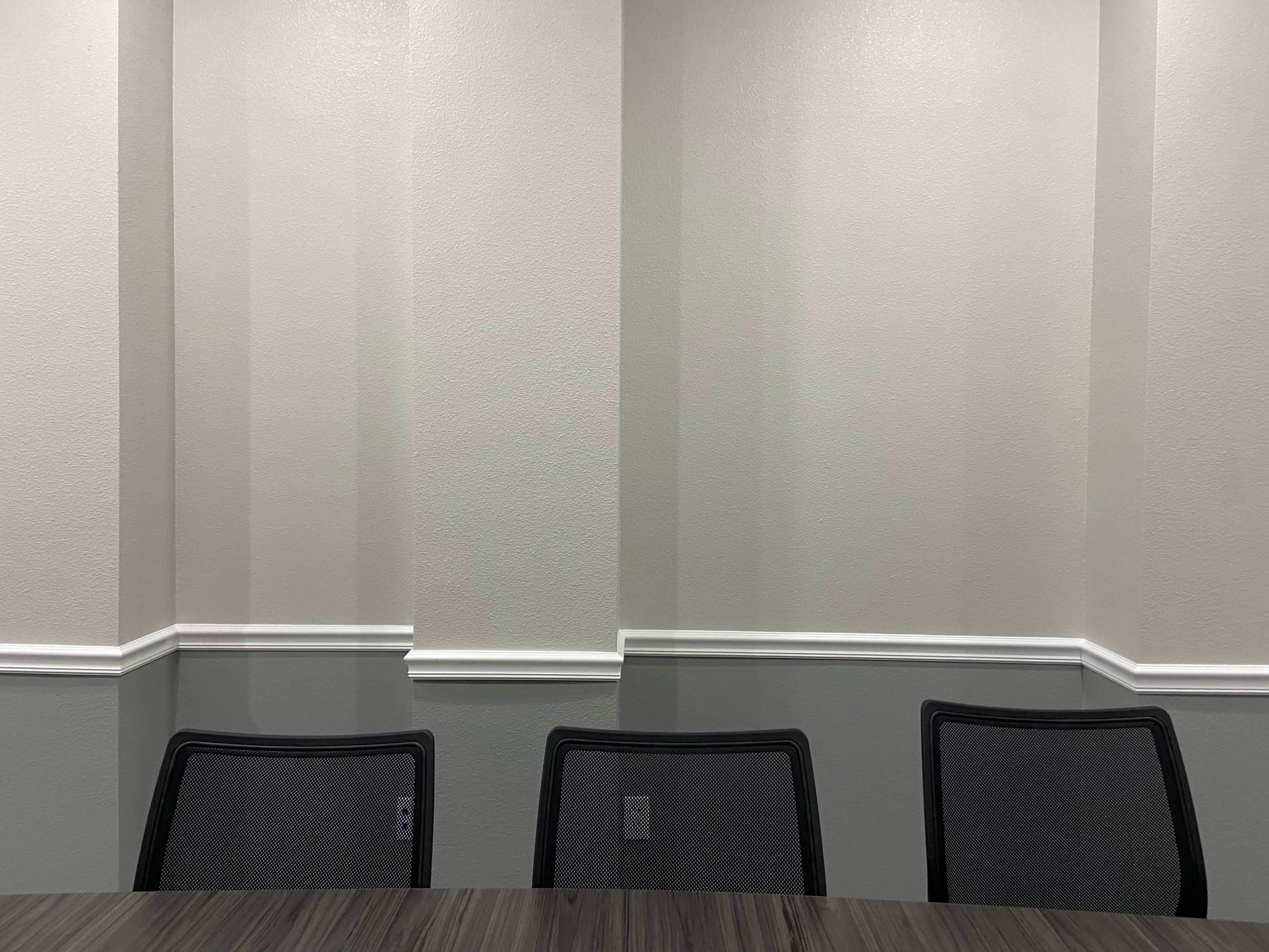 A meeting room with three empty chairs facing a plain, light-colored wall.