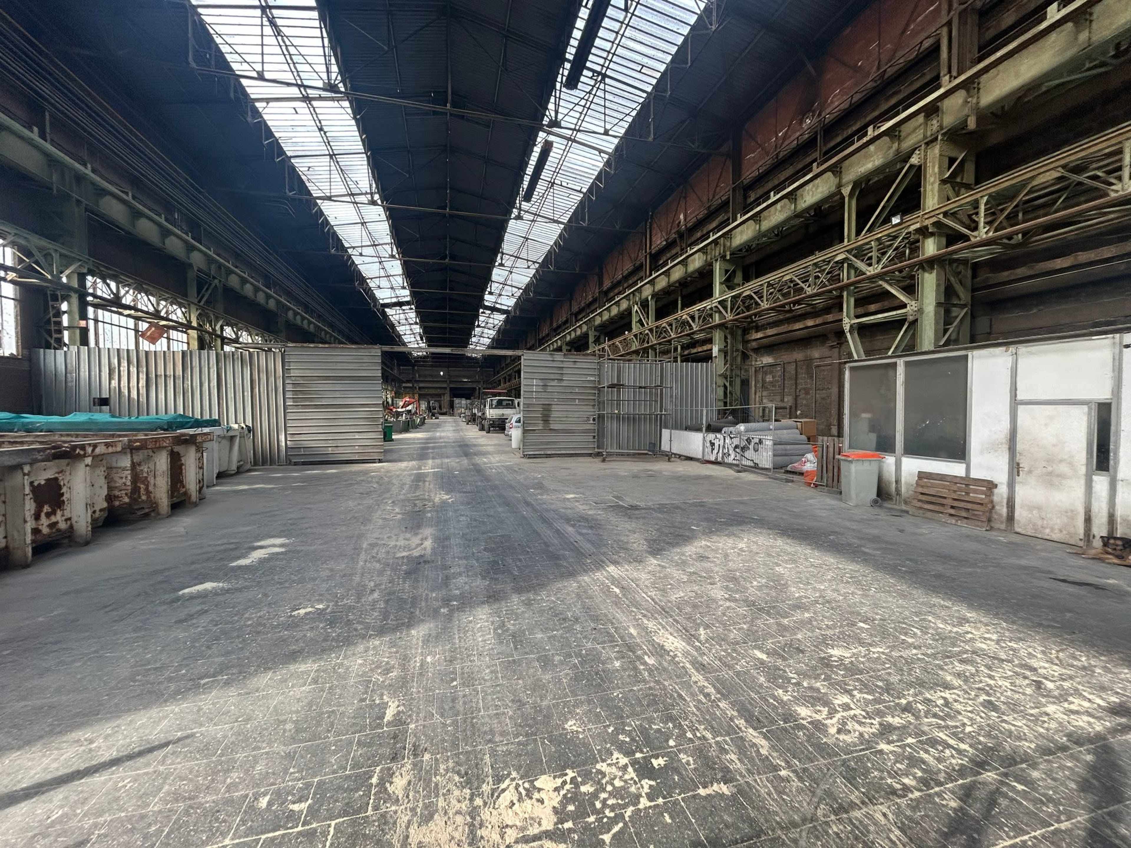 The interior of a large, empty industrial warehouse with tall ceilings and a visible row of metal container units on one side.