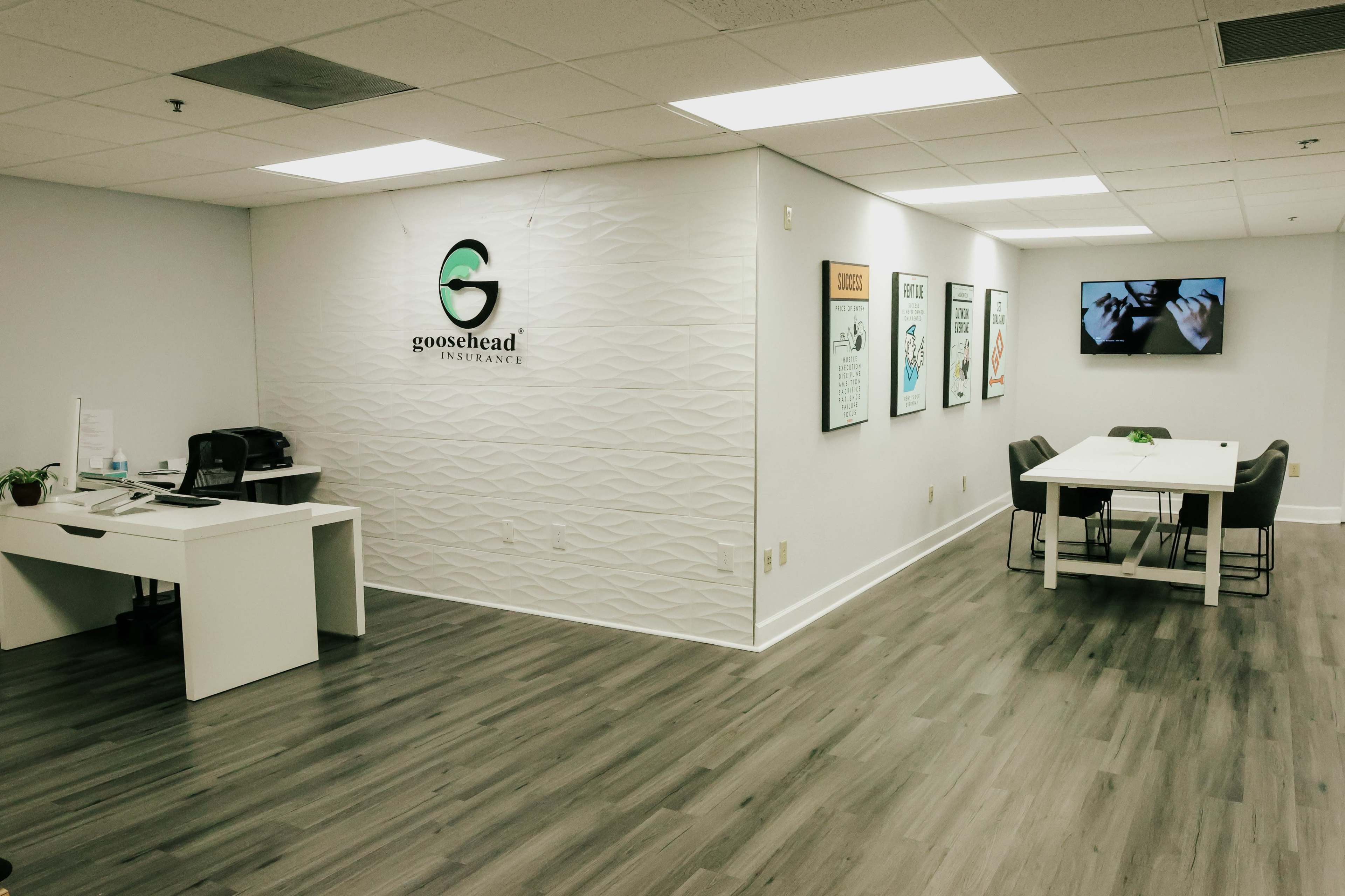 A modern office space for Goosehead Insurance, featuring a reception area with a desk and a conference room with a table and chairs.