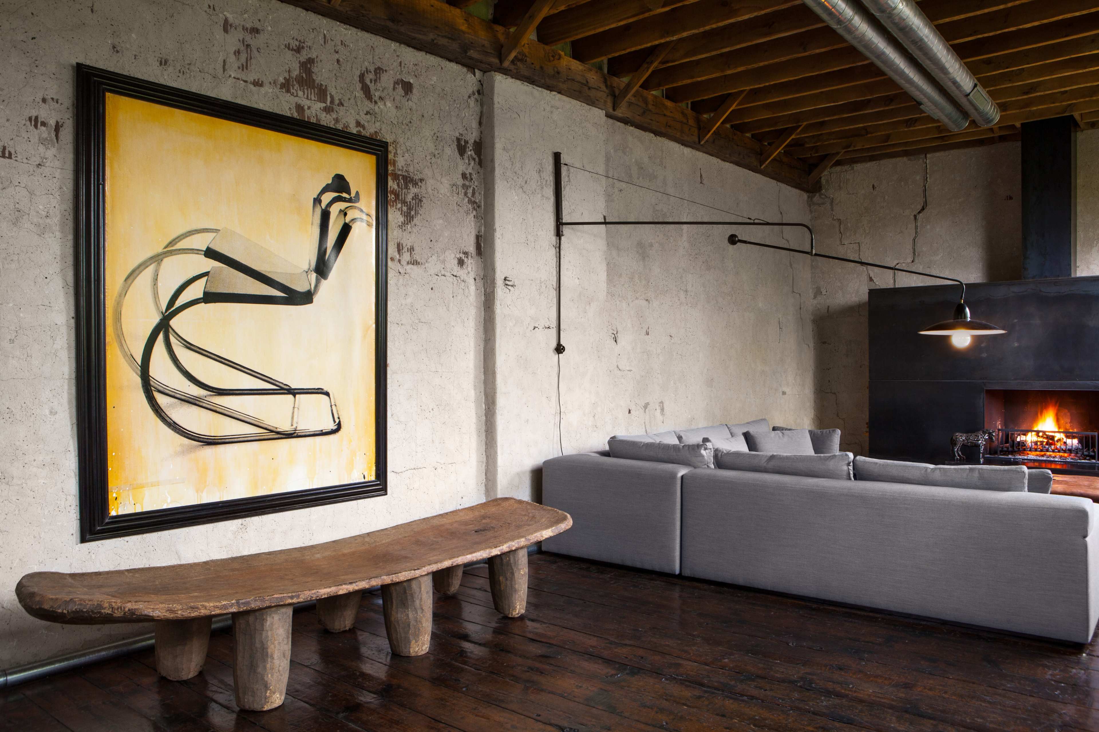A modern living room with a large abstract painting on the wall, a wooden coffee table, a gray sofa, and a fireplace.