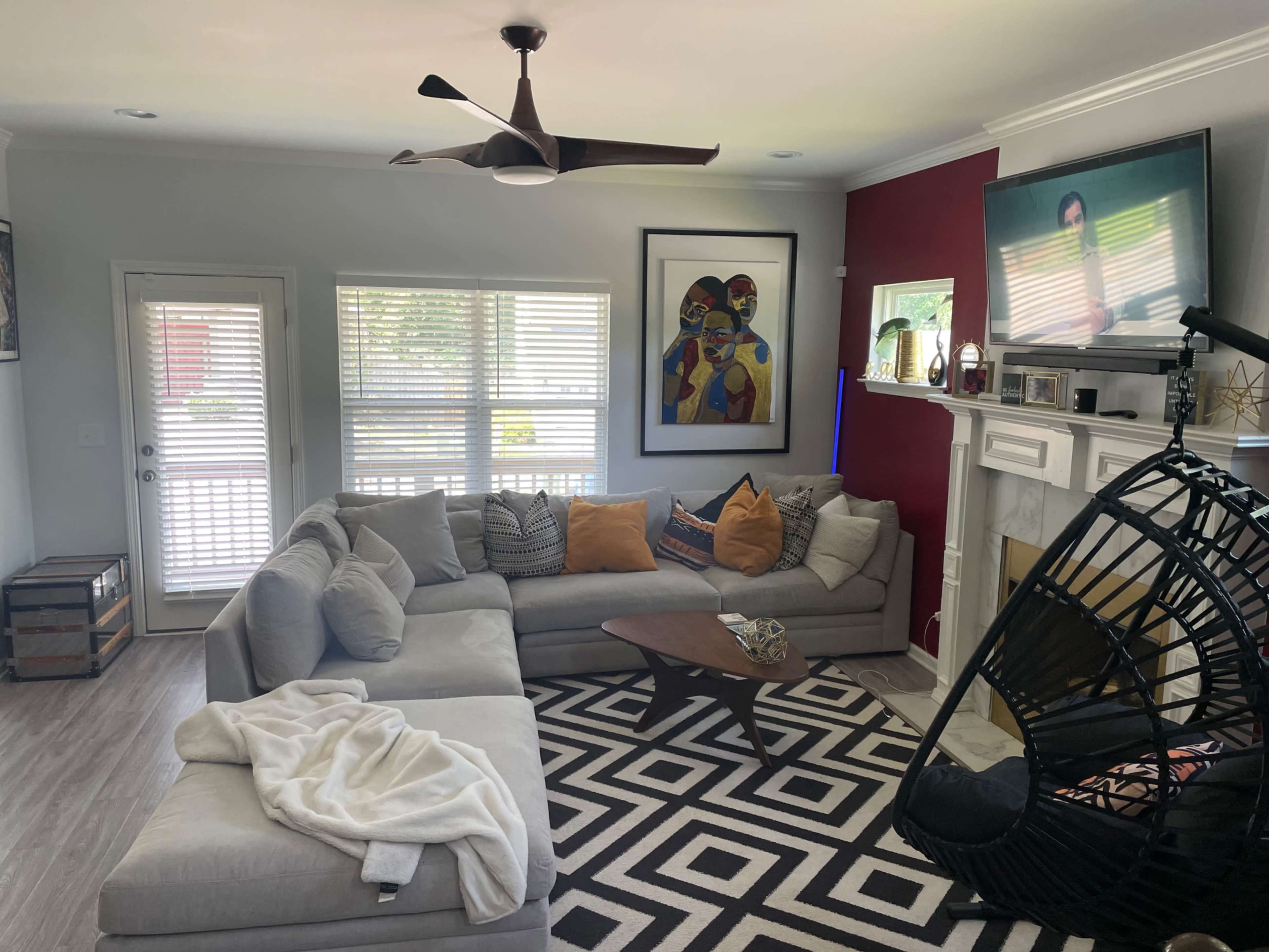The living room features a large sectional sofa, a wooden coffee table, a swing chair, and a wall-mounted television, all arranged around a geometric patterned rug.