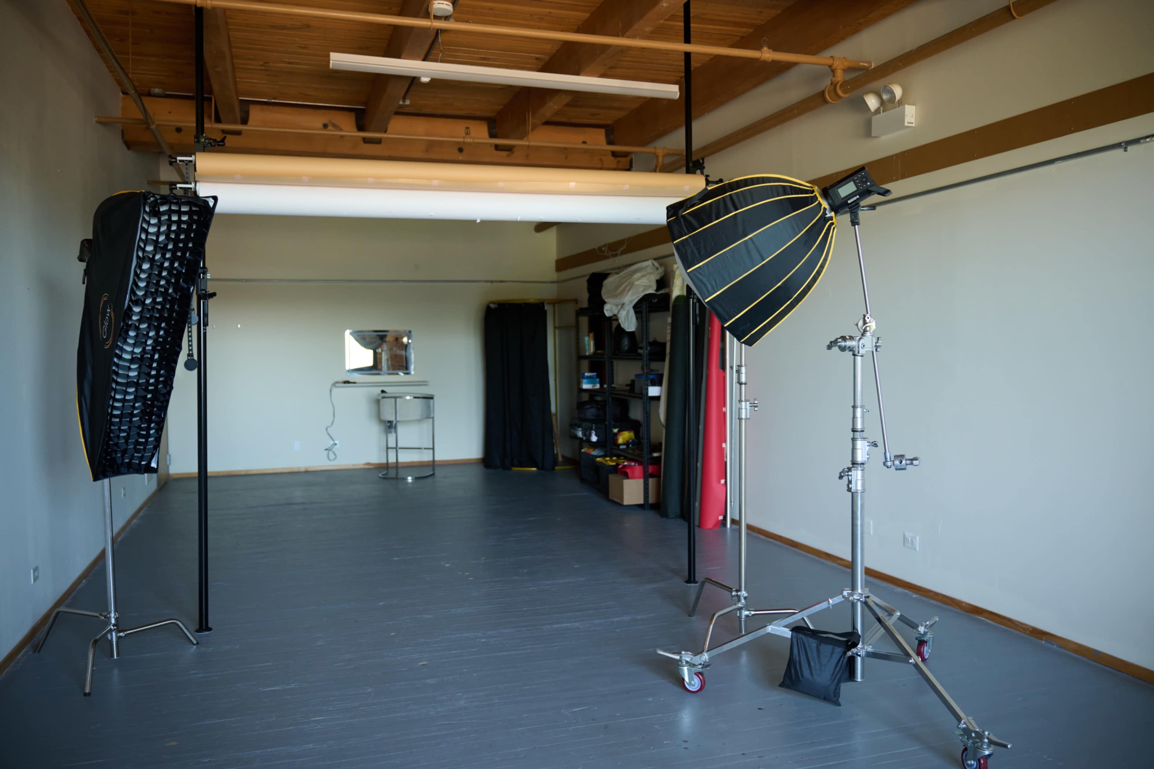 The image shows a photography studio with lighting equipment, a mirror, and storage items arranged along the walls.