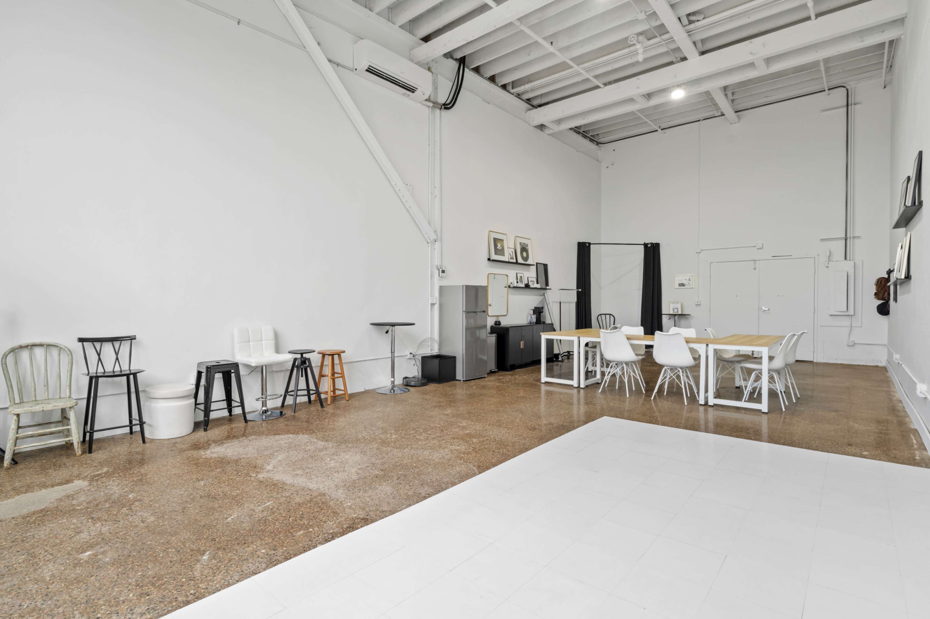 The image shows a spacious, minimalist room with various chairs and tables arranged on a polished floor.