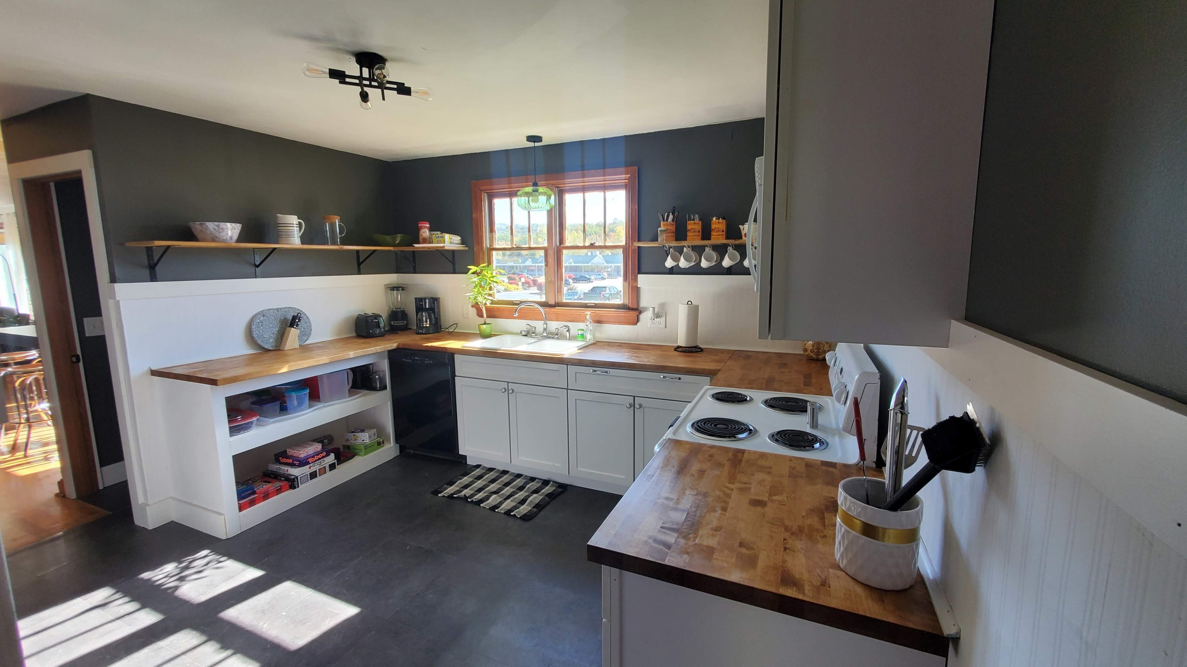 A kitchen with wooden countertops, white cabinetry, and a window above the sink, featuring a simple layout and a few decorative items on shelves.