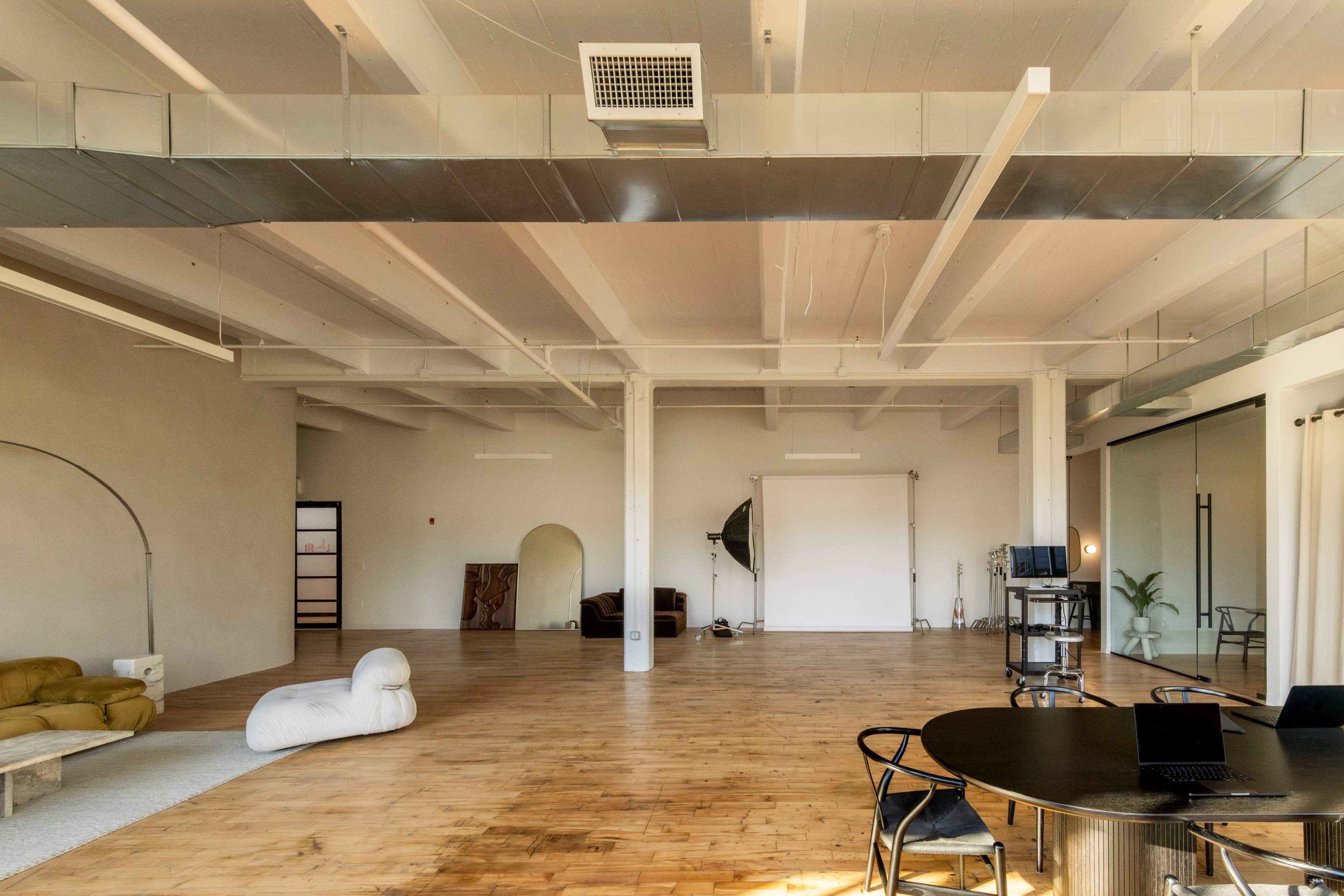 The image depicts a spacious, empty interior of a modern office or studio with wooden flooring and minimalistic furniture.