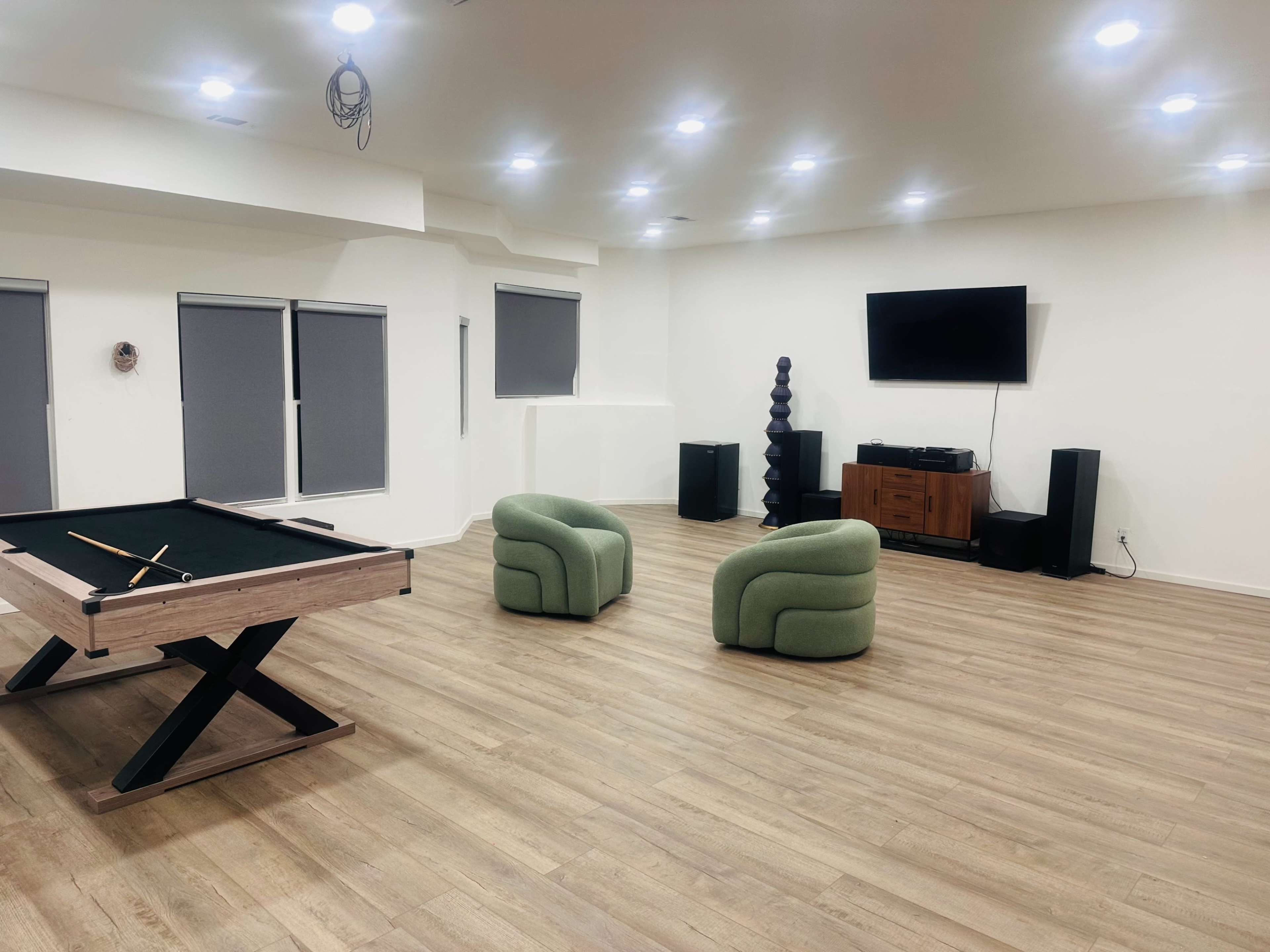 The image shows a spacious game room featuring a billiard table, two green chairs, a television on the wall, and a wooden cabinet.