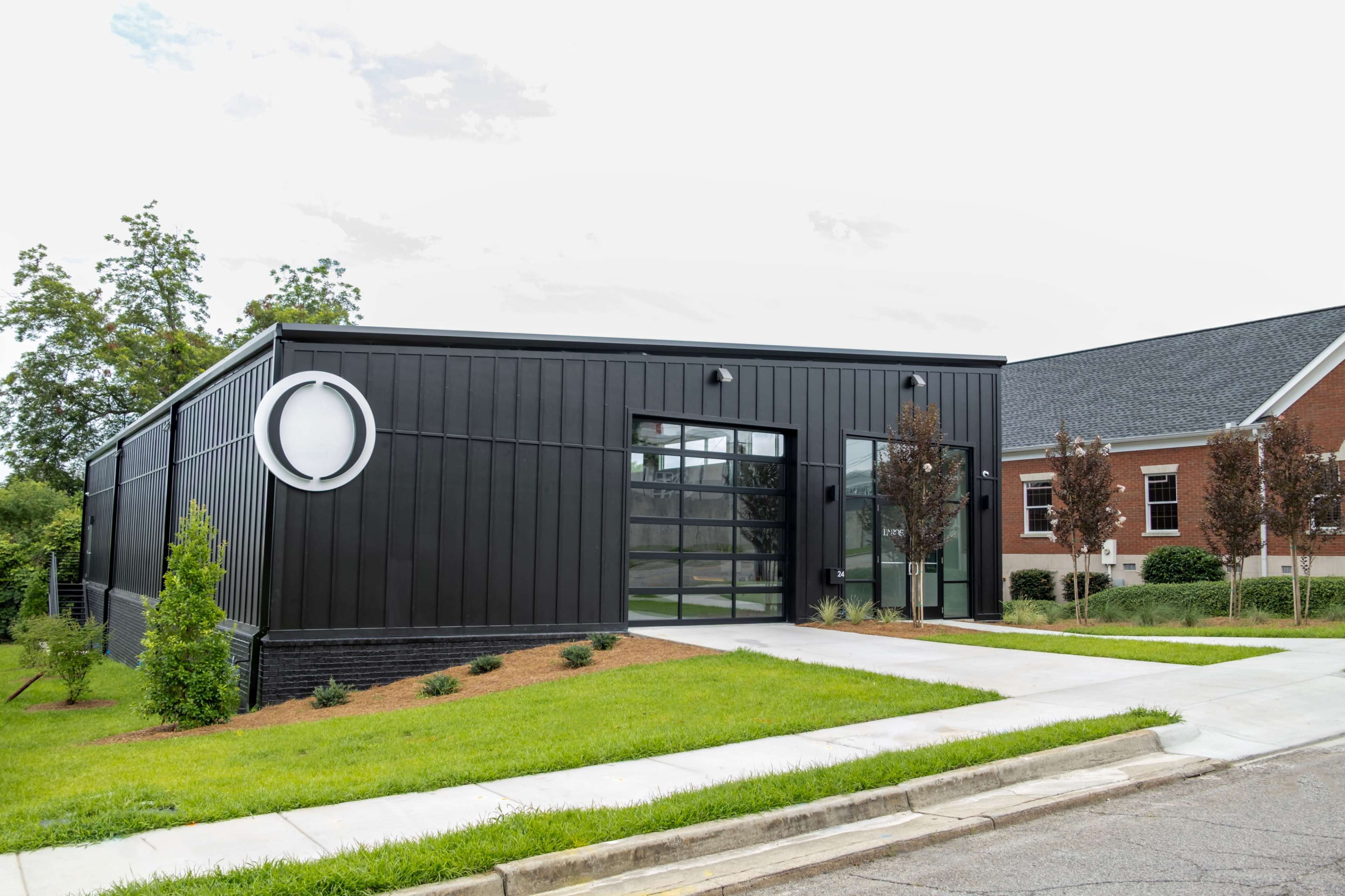 The image shows a modern black building with large windows and a circular design element, located next to a traditional brick structure.