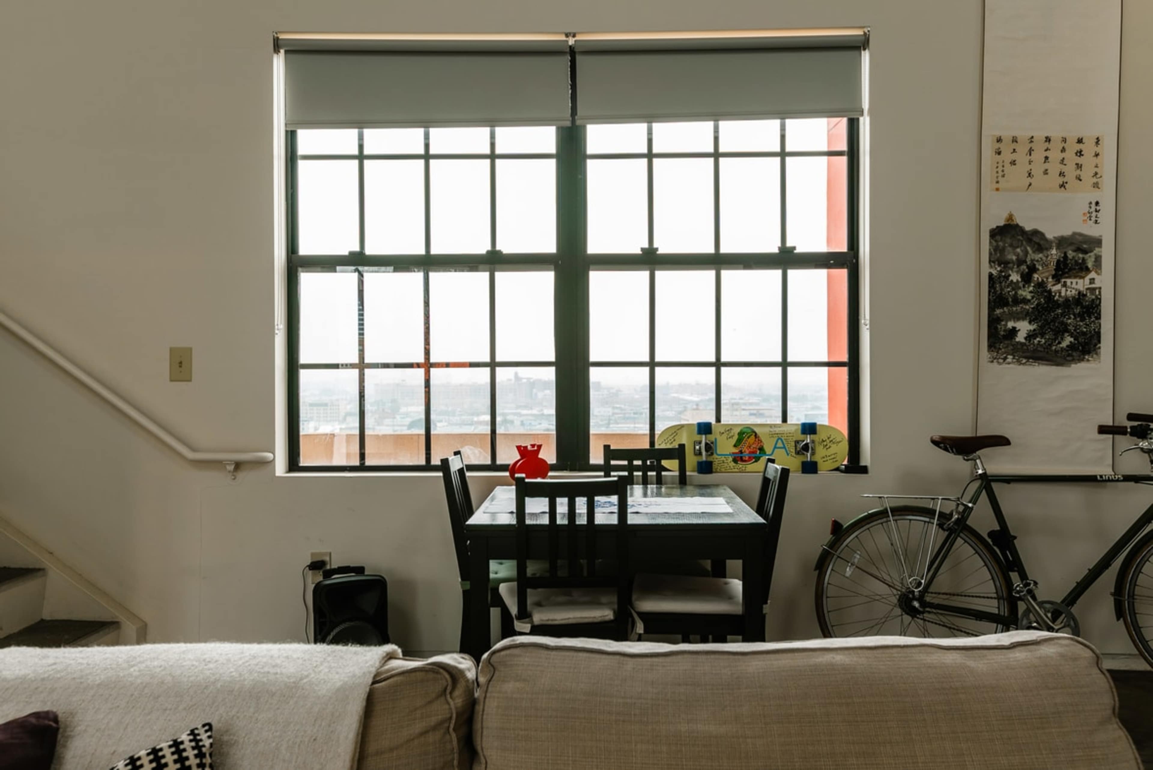 A dining area features a table with four chairs beside a large window with multiple panes, and a bicycle is parked against the wall.