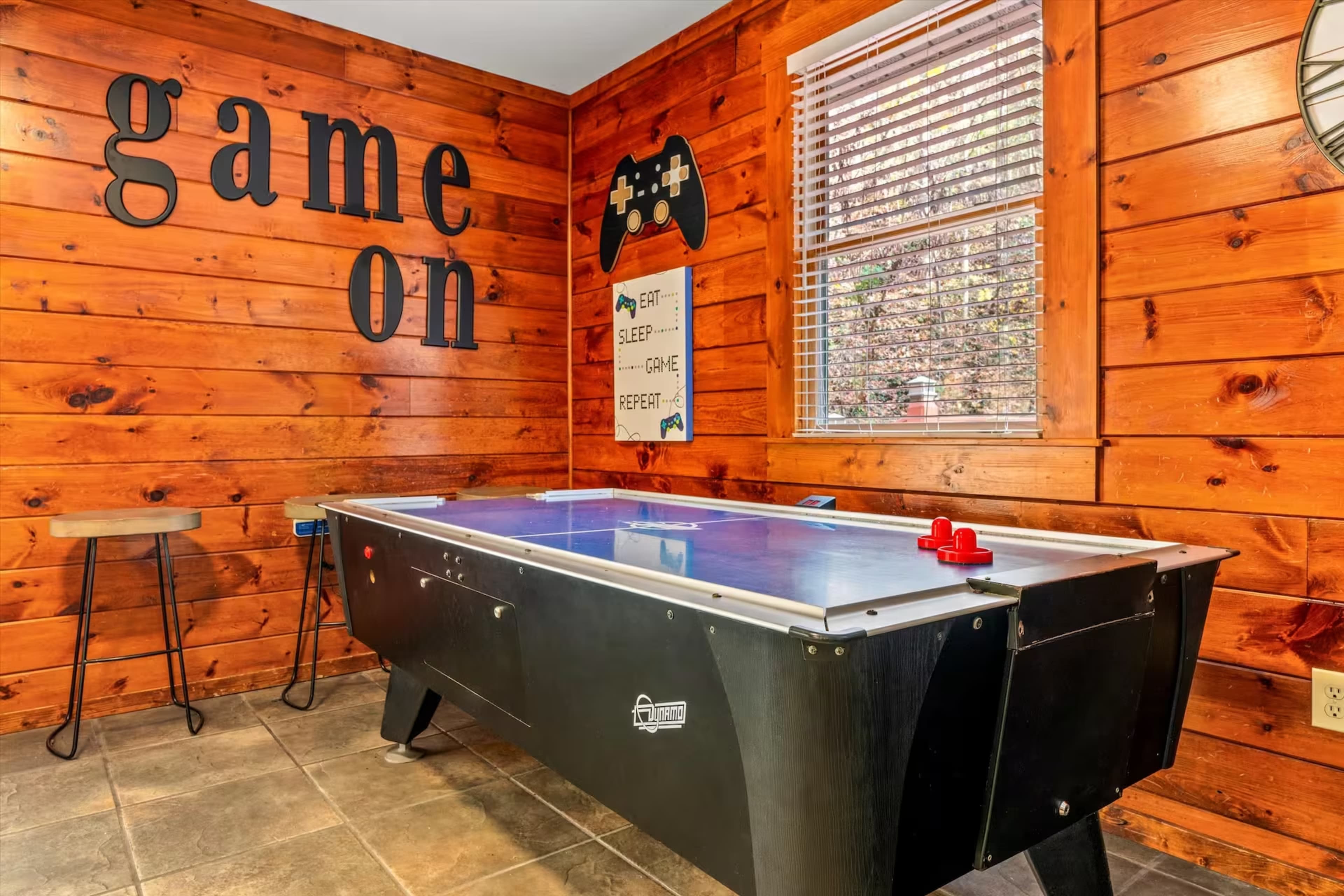 The image shows a game room with a black air hockey table, wooden paneling on the walls, and a "game on" sign.