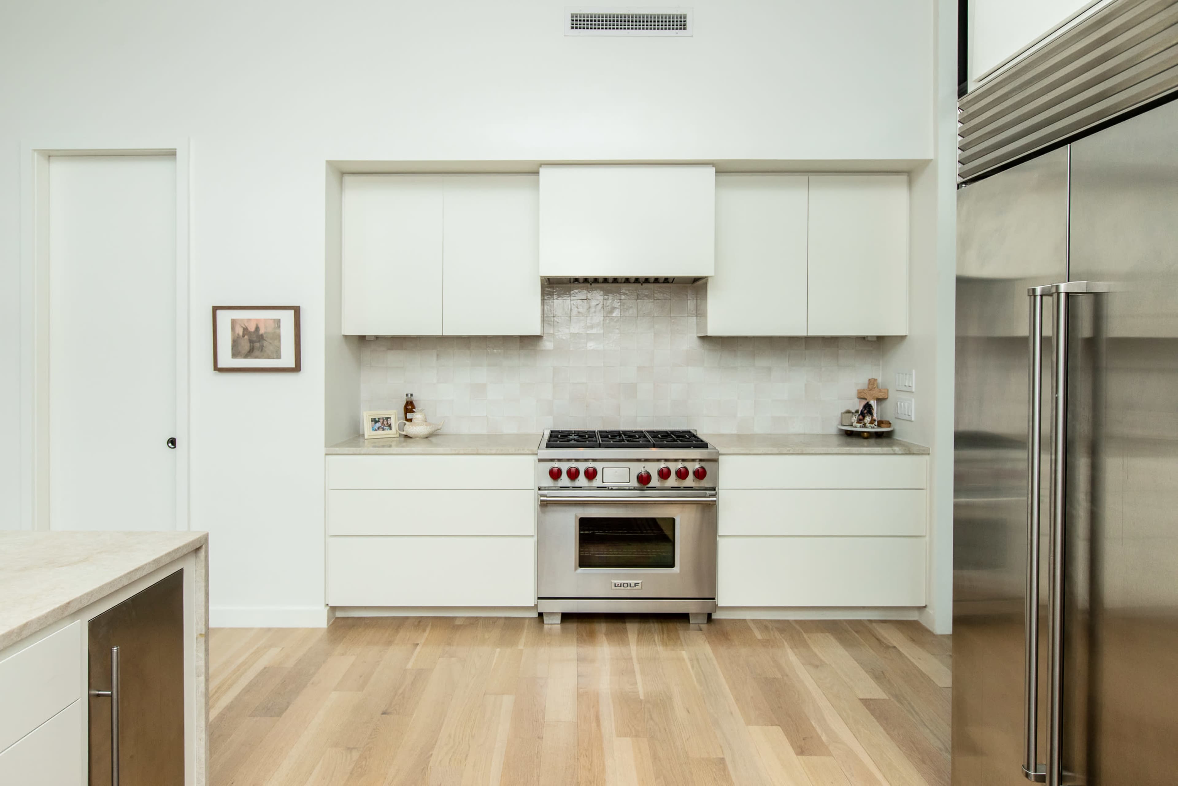 A modern kitchen with white cabinetry, a stainless steel refrigerator, and a gas range with red knobs.