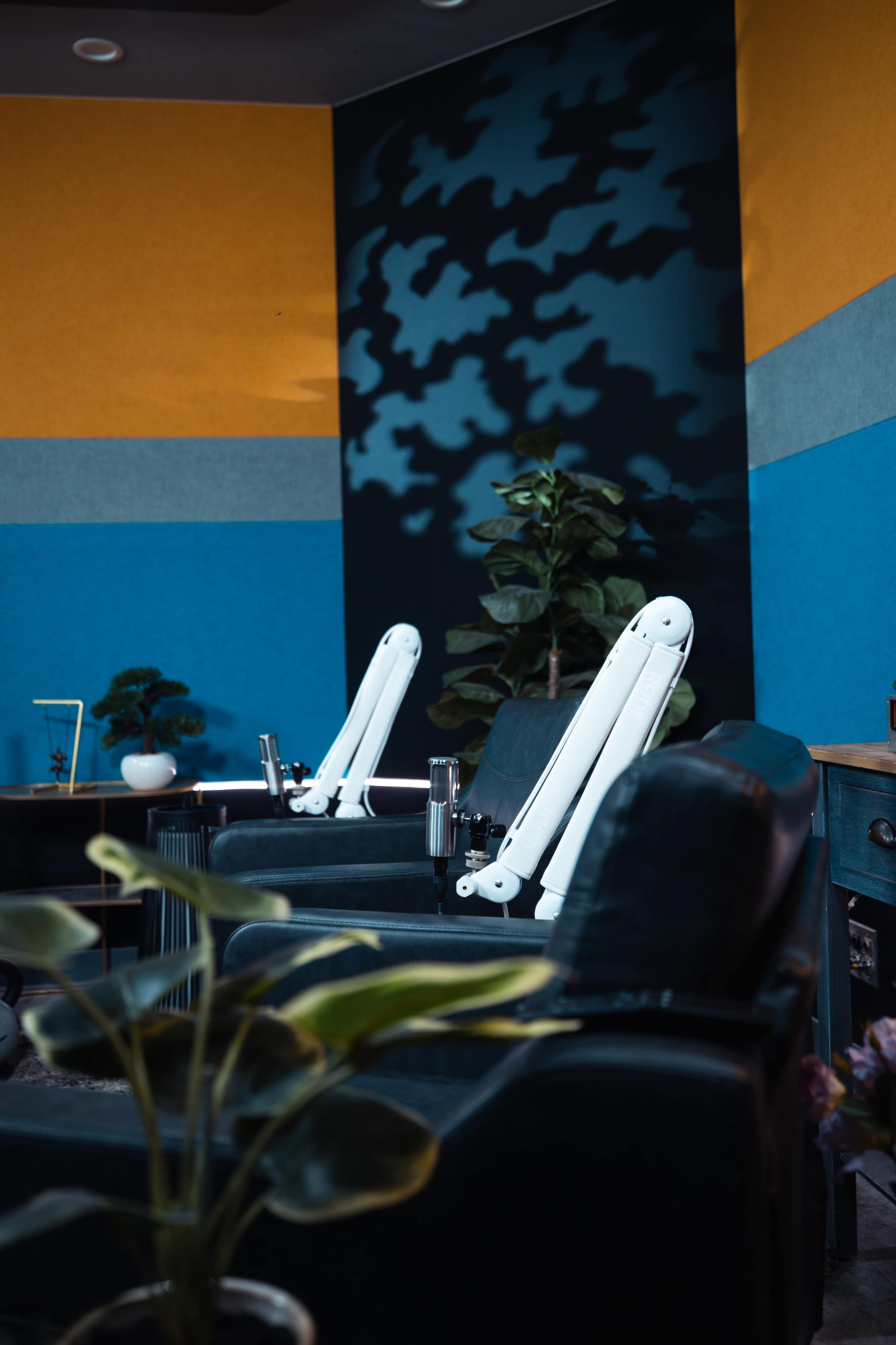 The image shows two modern salon chairs with adjustable footrests in a colorful interior designed for a spa or salon, along with a potted plant and decorative elements in the background.