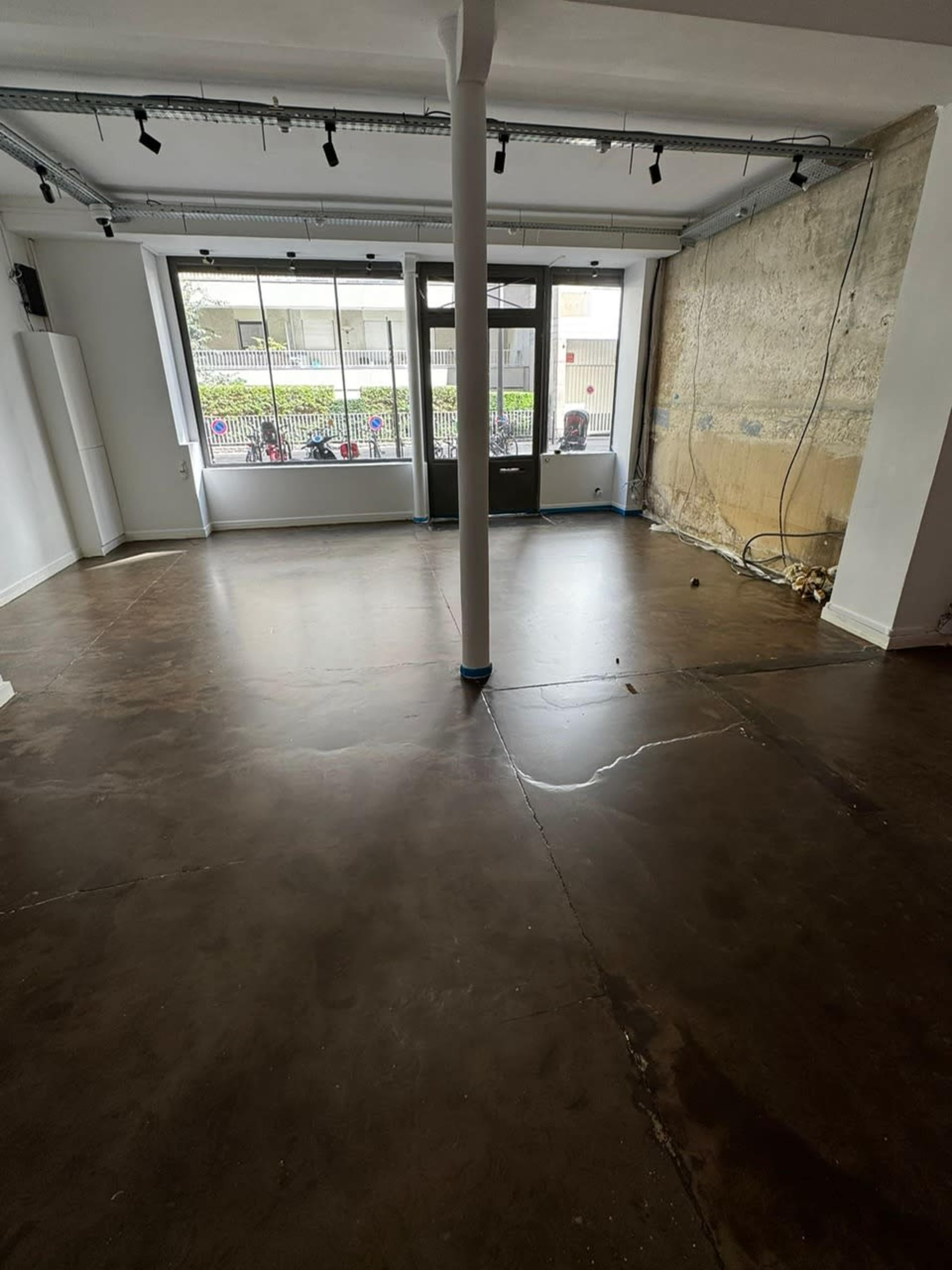 The image shows an empty room with a polished concrete floor, a large window at the front, and exposed walls on one side.