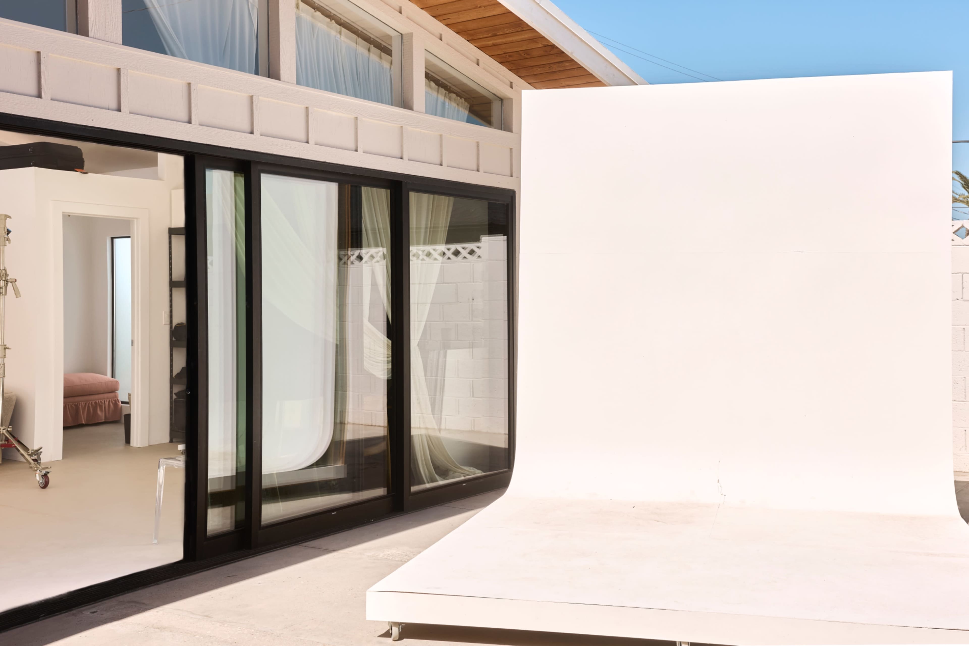 The image shows a modern outdoor space featuring a large white backdrop near a glass wall of a house with curtains.