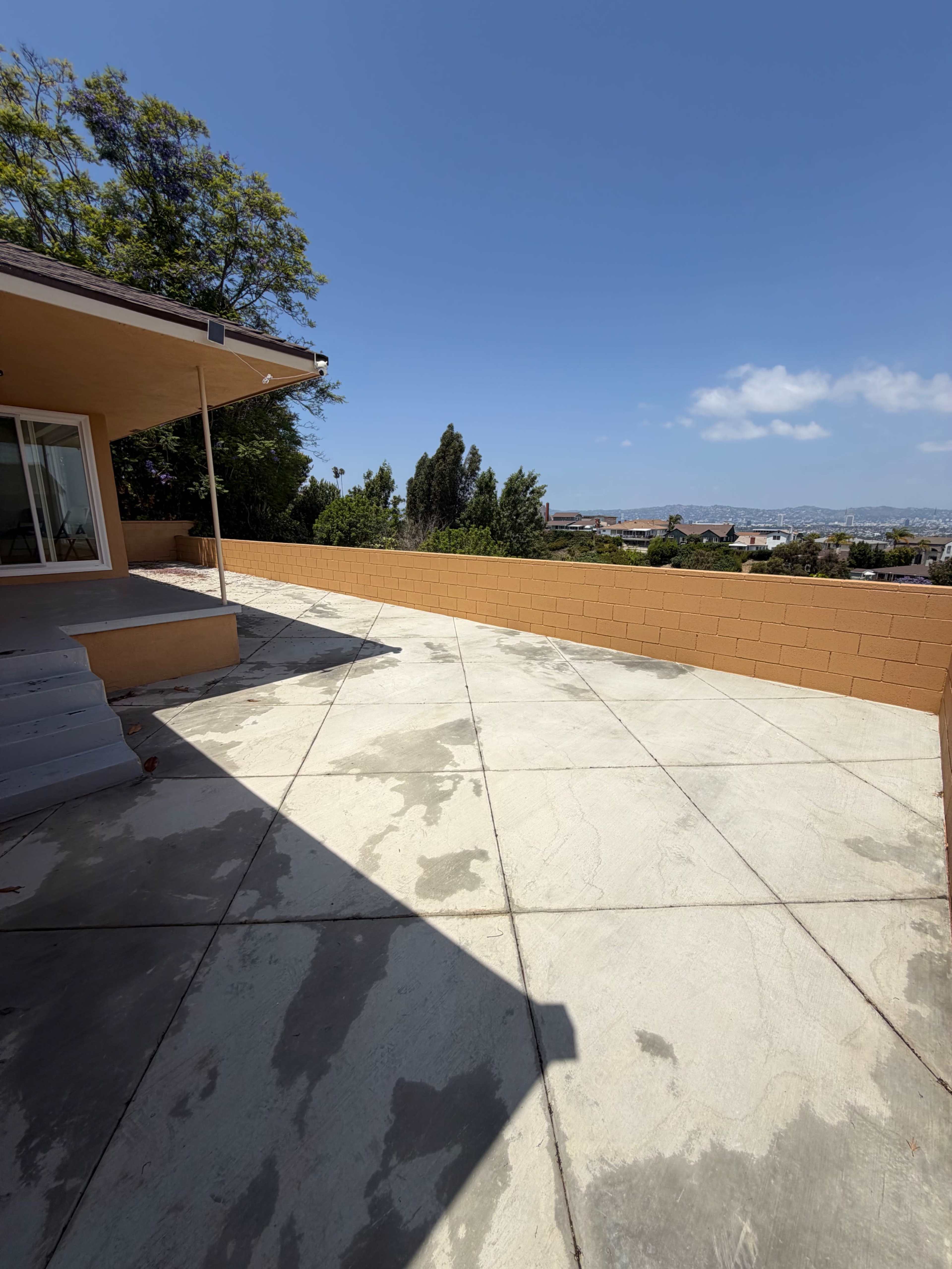 The image shows a concrete patio area next to a house, with a low wall separating it from a view of the landscape and sky.
