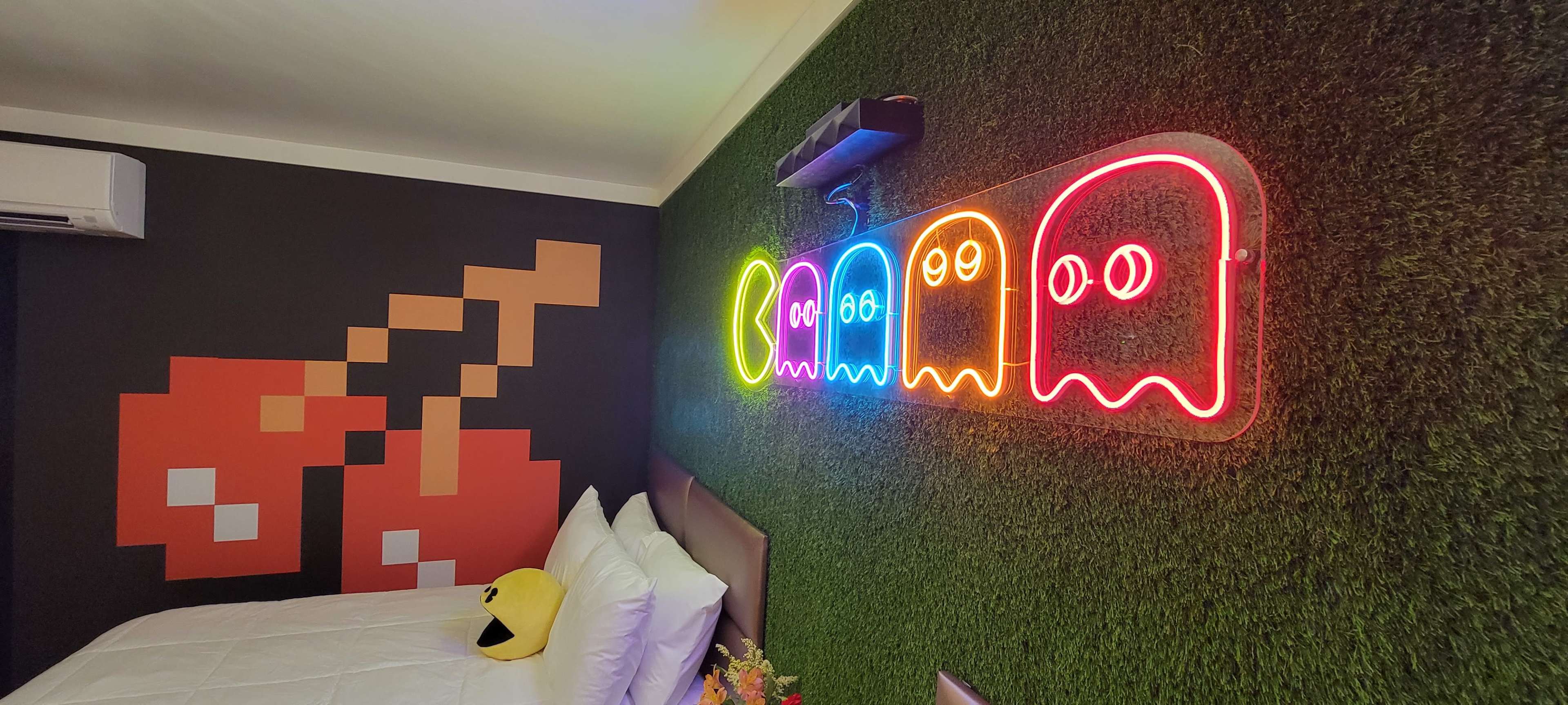 The image shows a colorful, retro-themed bedroom featuring a neon ghost light display on a green grass-like wall, with pixel art cherries and a yellow smiley face on the bed.