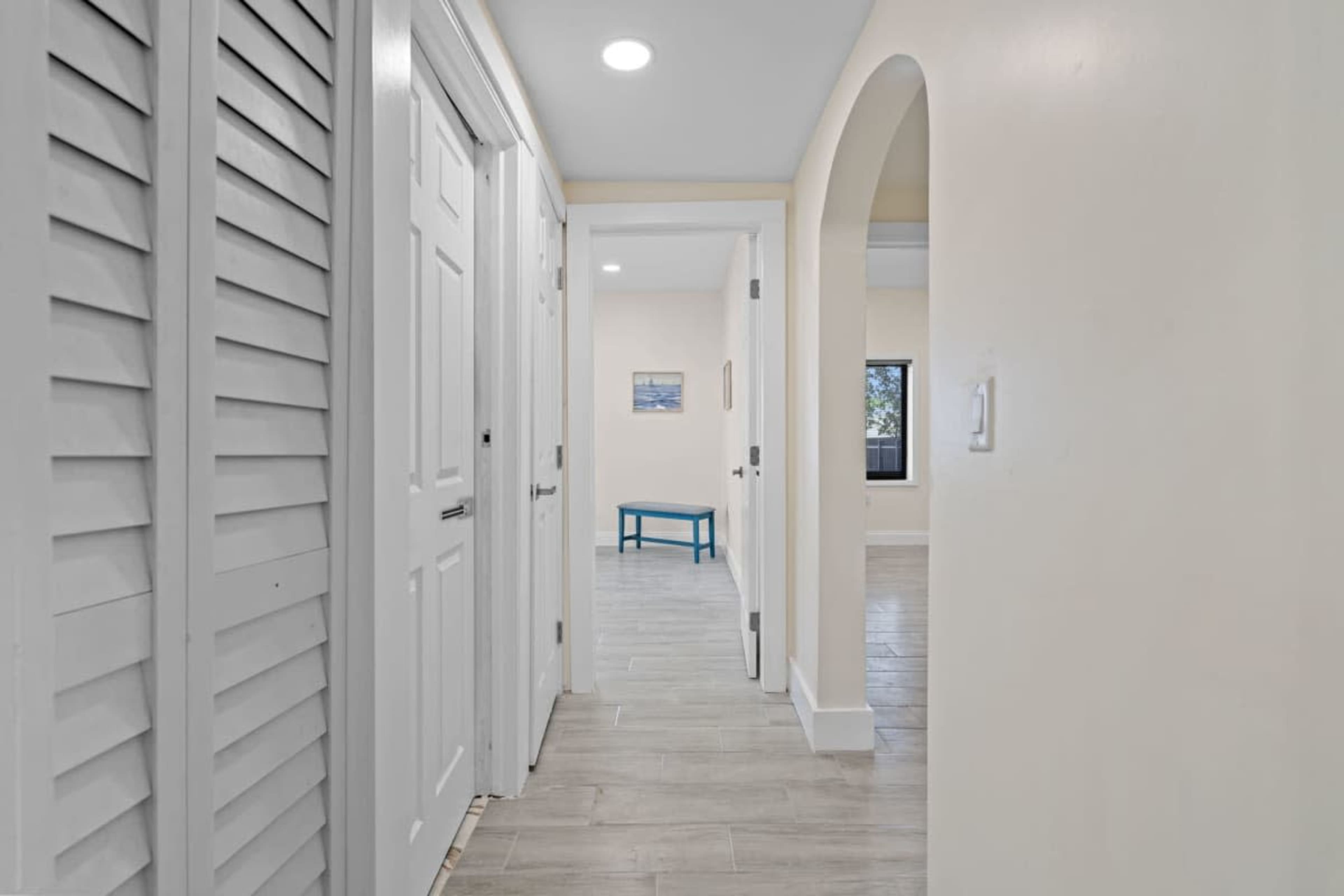 The image depicts a well-lit hallway with white doors and walls, leading to an open space featuring a small blue table.