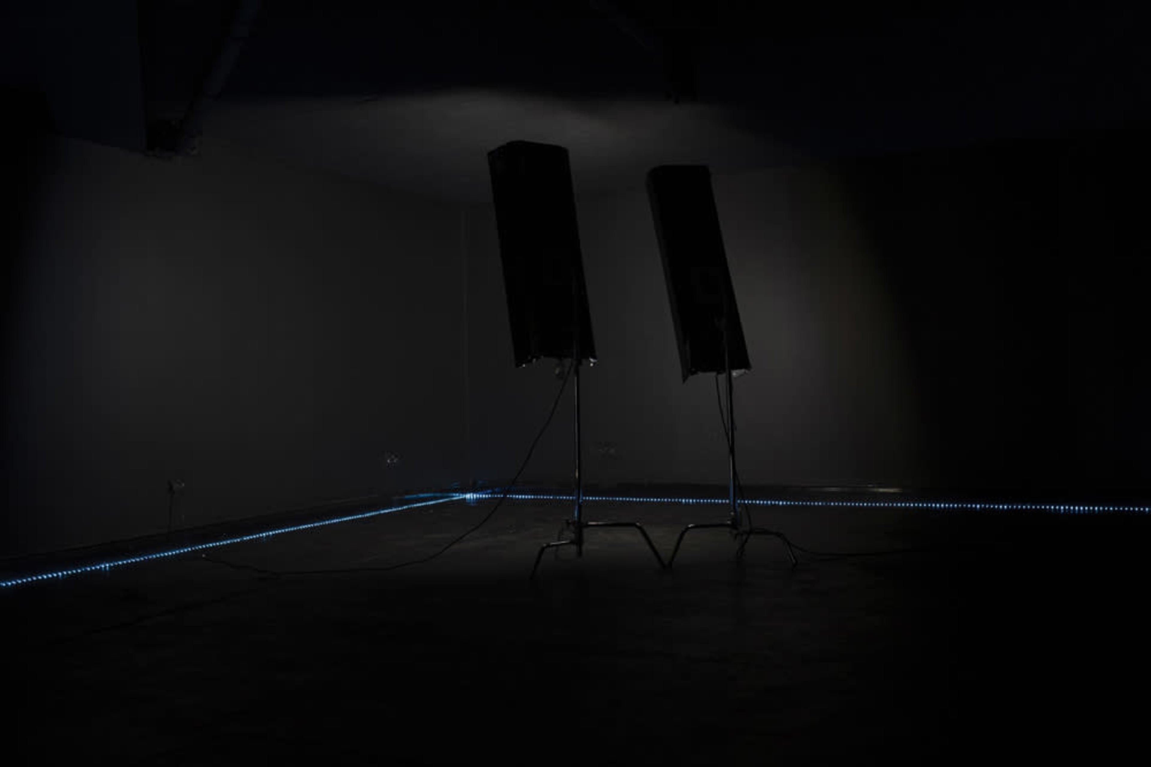 Two tall speakers stand in a dimly lit room with a LED light strip along the floor.