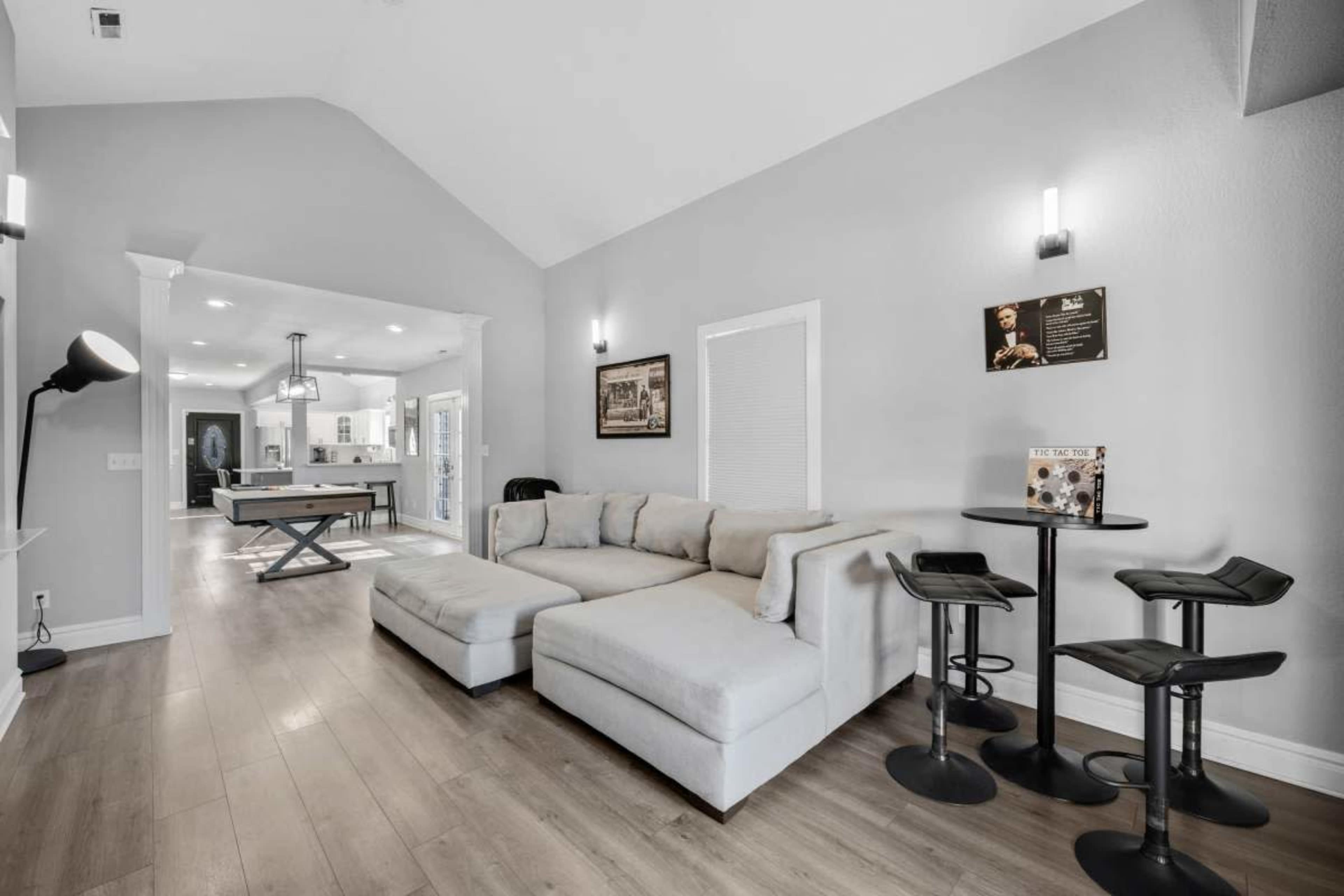 A light-colored living room with a sectional sofa, bar seating, and an open view into a kitchen area.