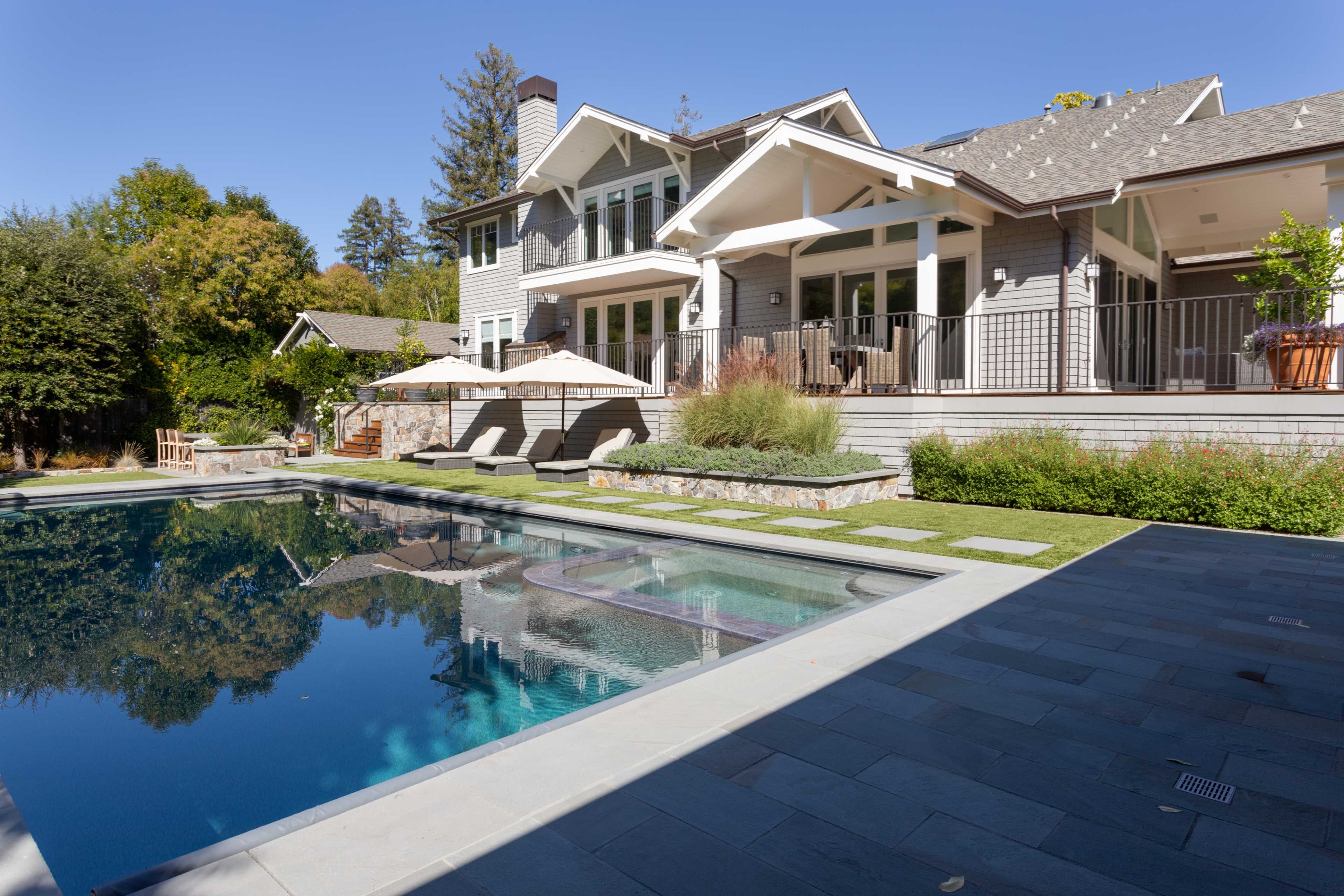 A modern house with a backyard pool is surrounded by landscaped greenery and outdoor furniture.