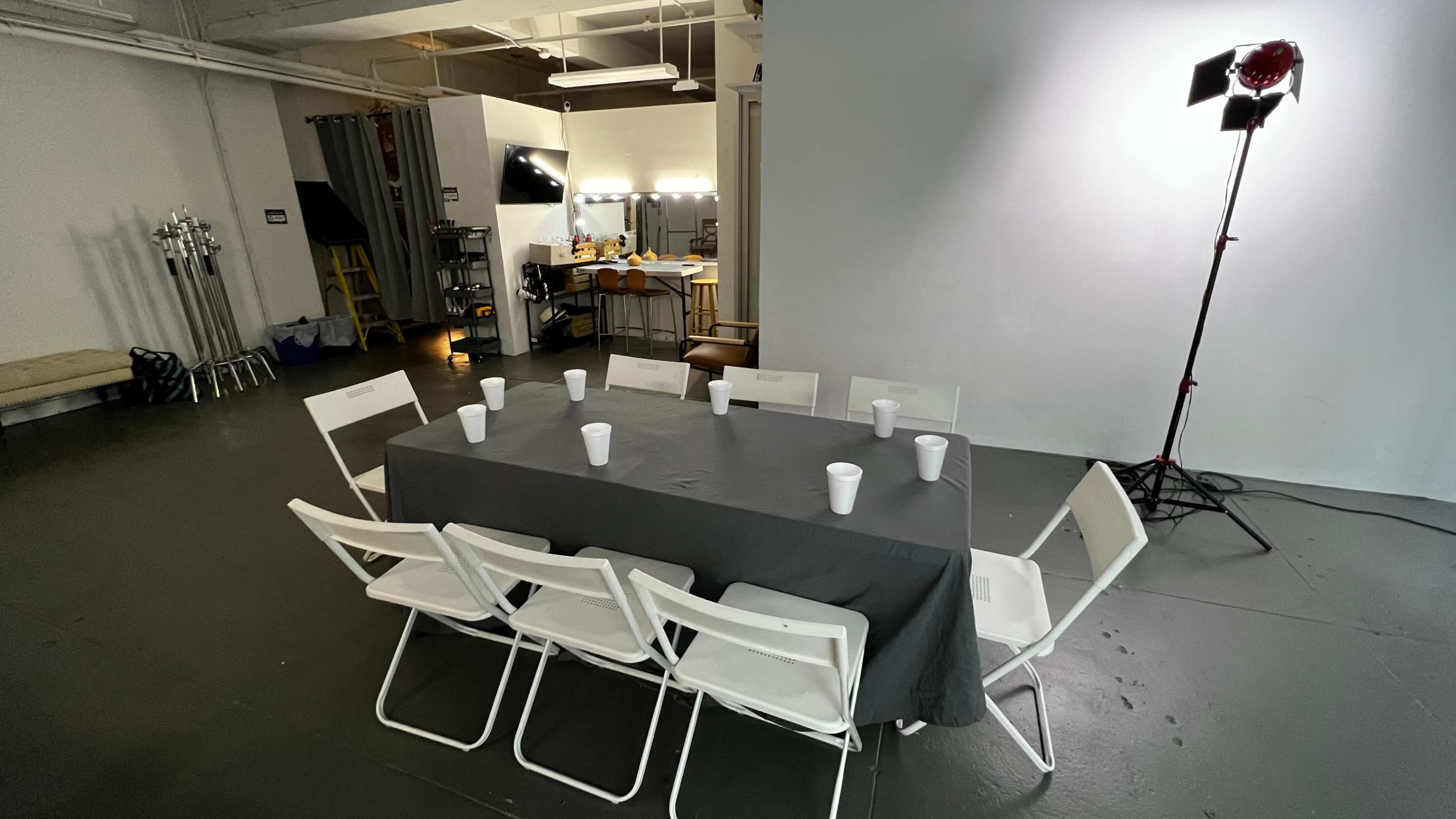 A table covered with a gray cloth is set up in a studio, surrounded by white chairs and small cups placed on the table.