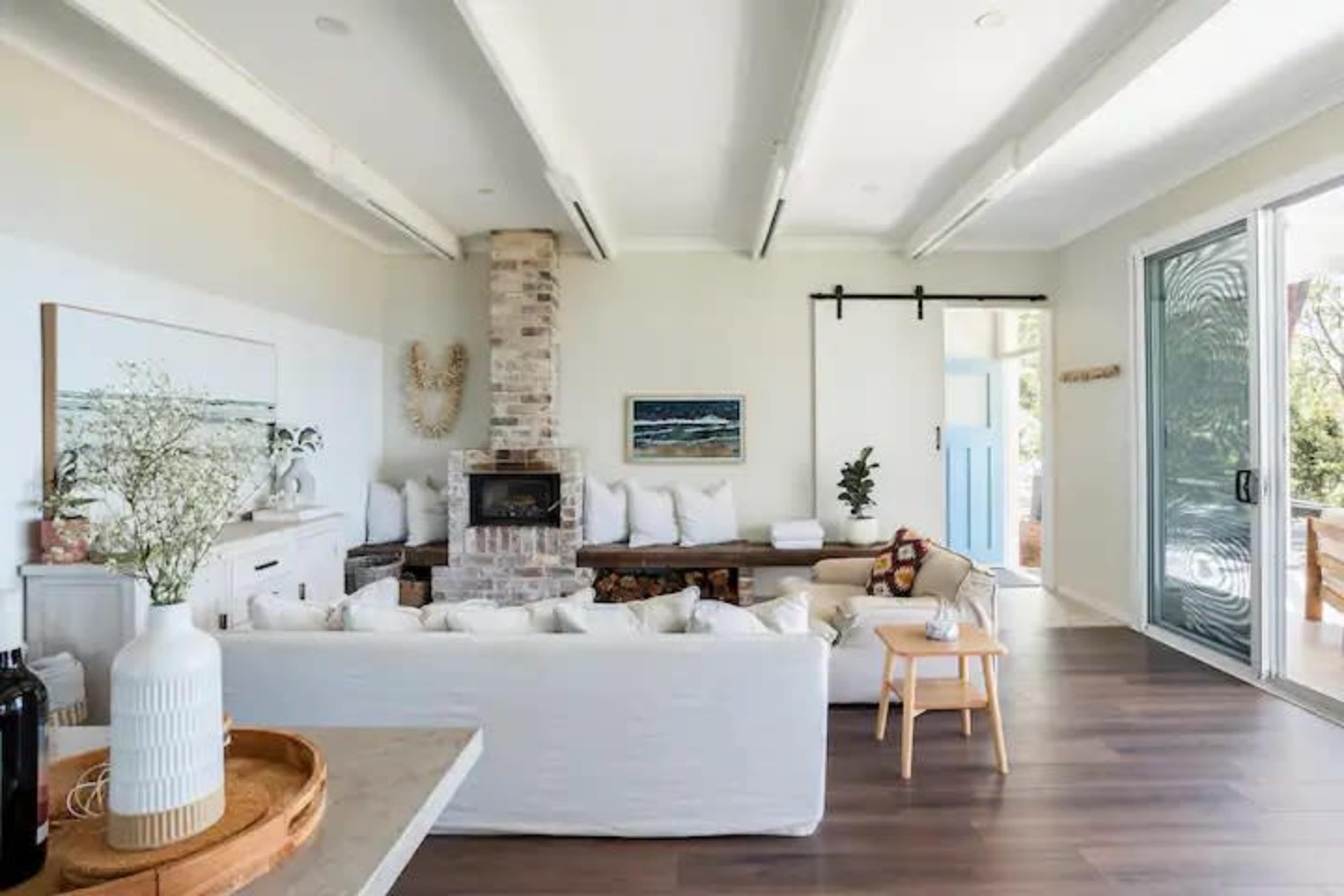 A bright living room featuring a brick fireplace, a large white sofa, and a blue door that opens to an outdoor area.
