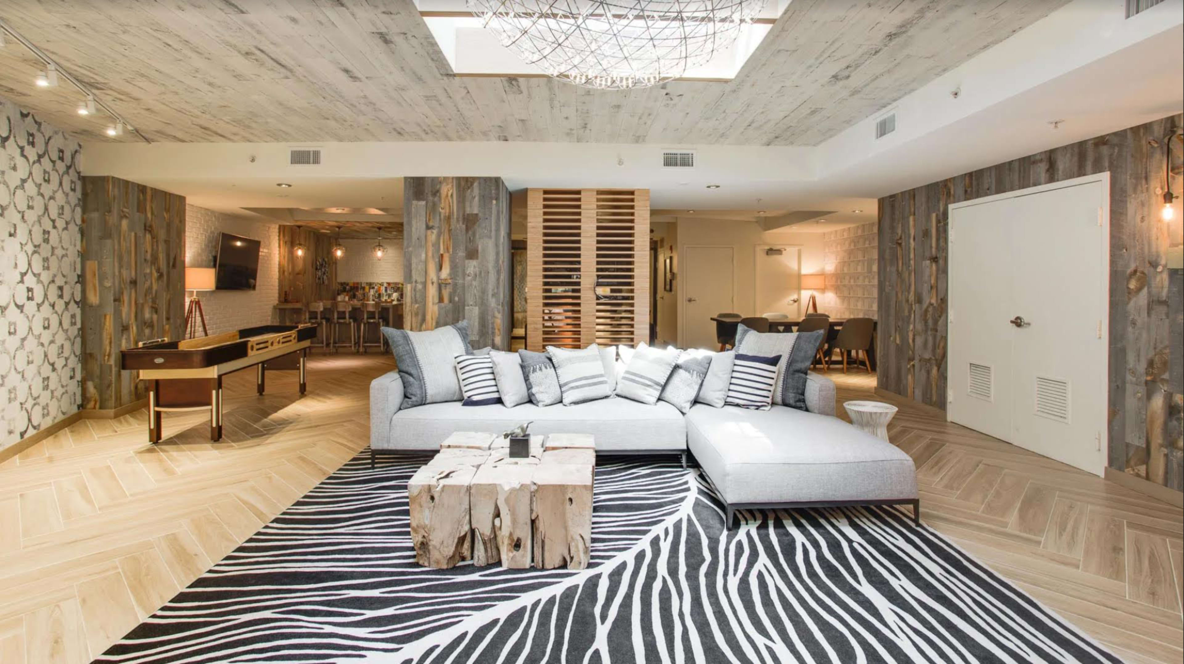 A spacious, modern living area featuring a light gray sectional sofa, a rustic wooden coffee table, and a striped black-and-white area rug.