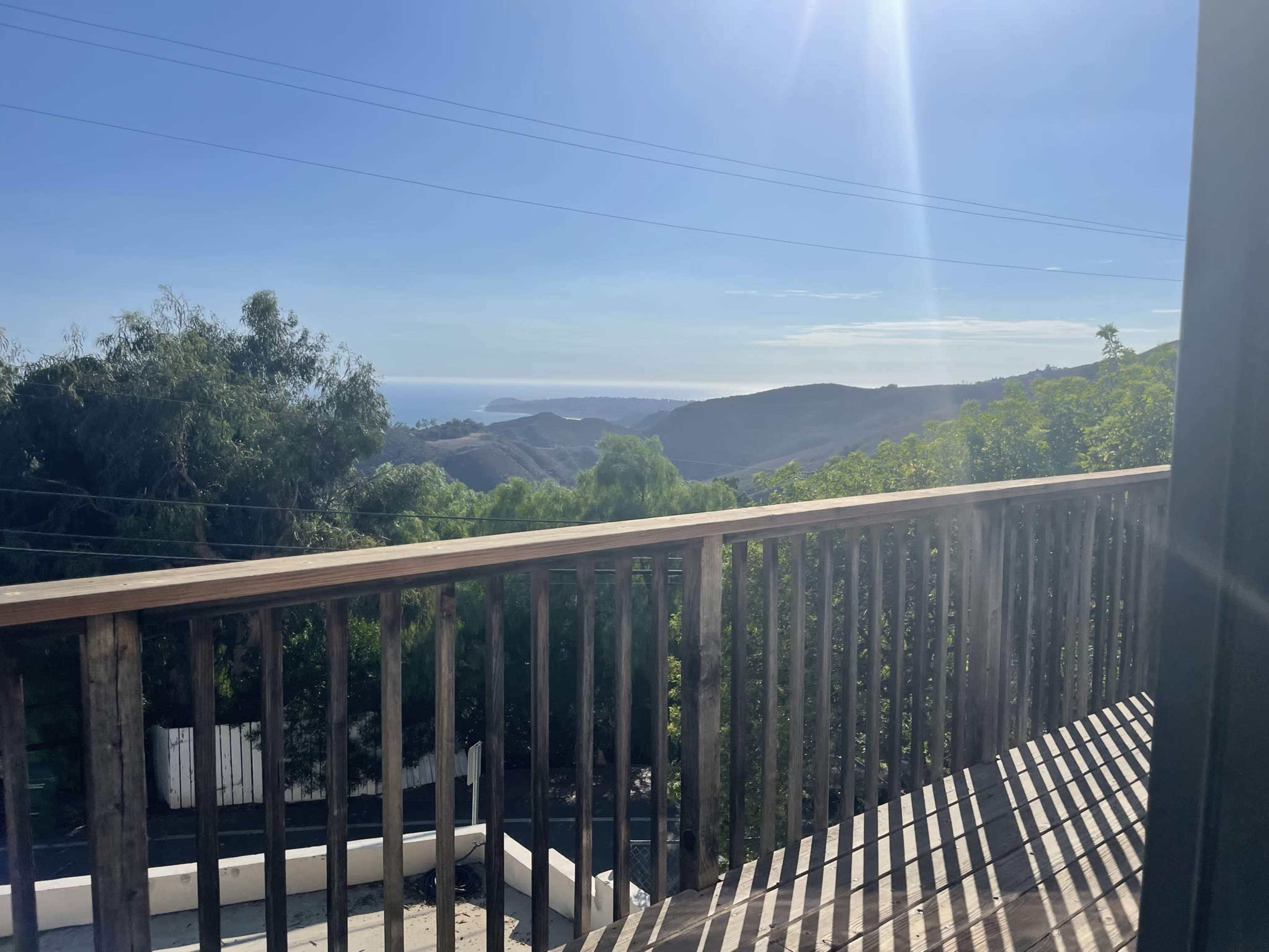 A wooden railing overlooking rolling hills and the ocean in the distance under a clear sky.