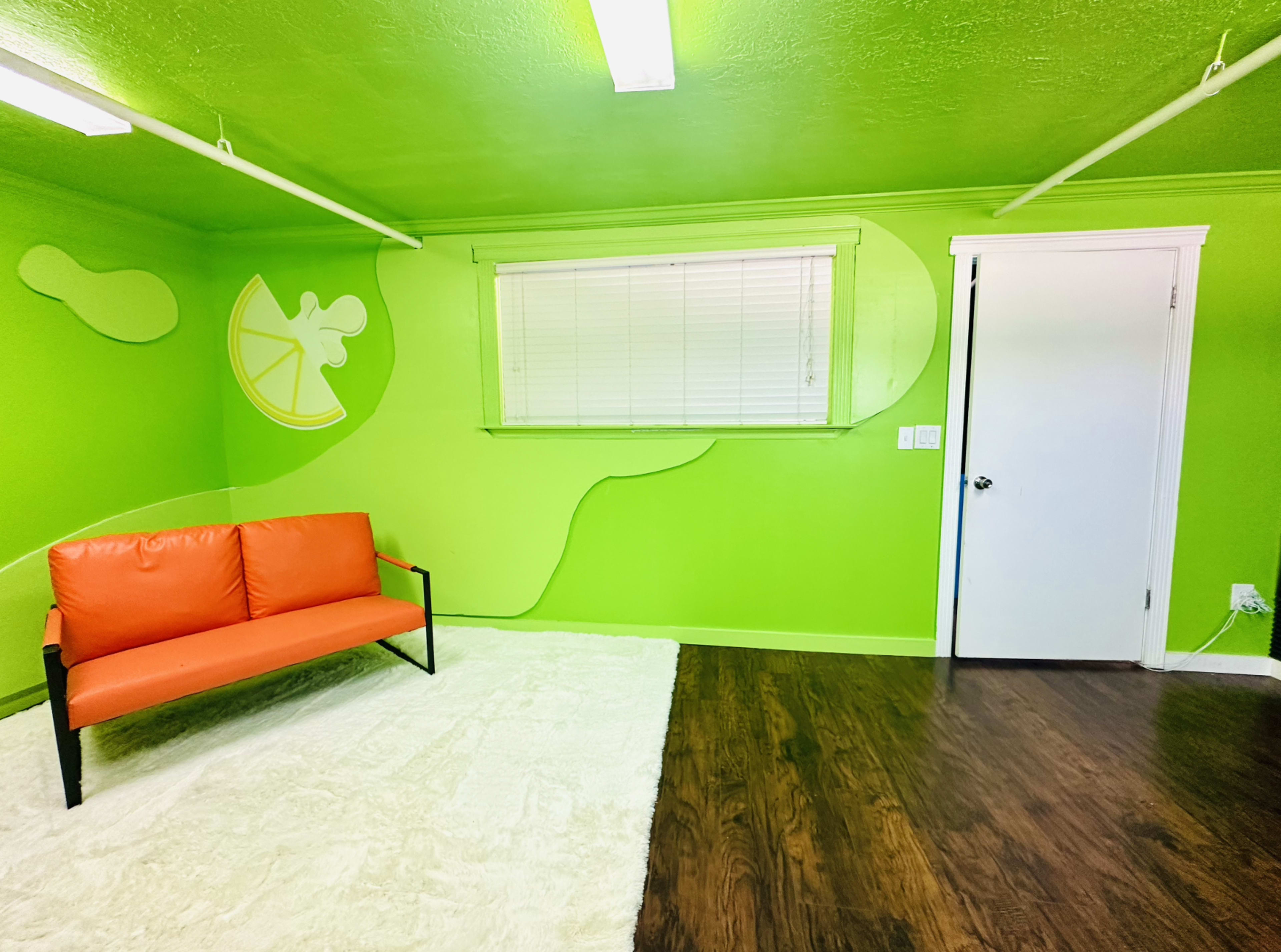 A bright green room features a textured wall design, an orange sofa, and a window with white blinds.