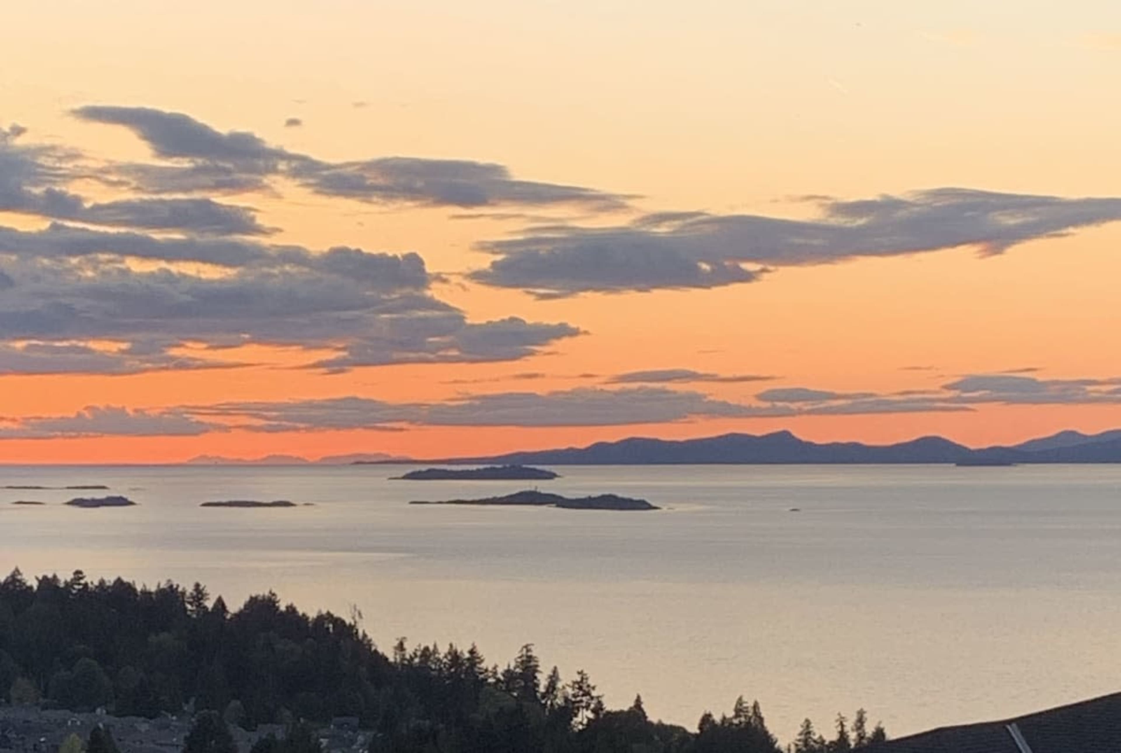A sunset over a body of water, with islands visible in the distance and a colorful sky reflecting orange and pink hues.