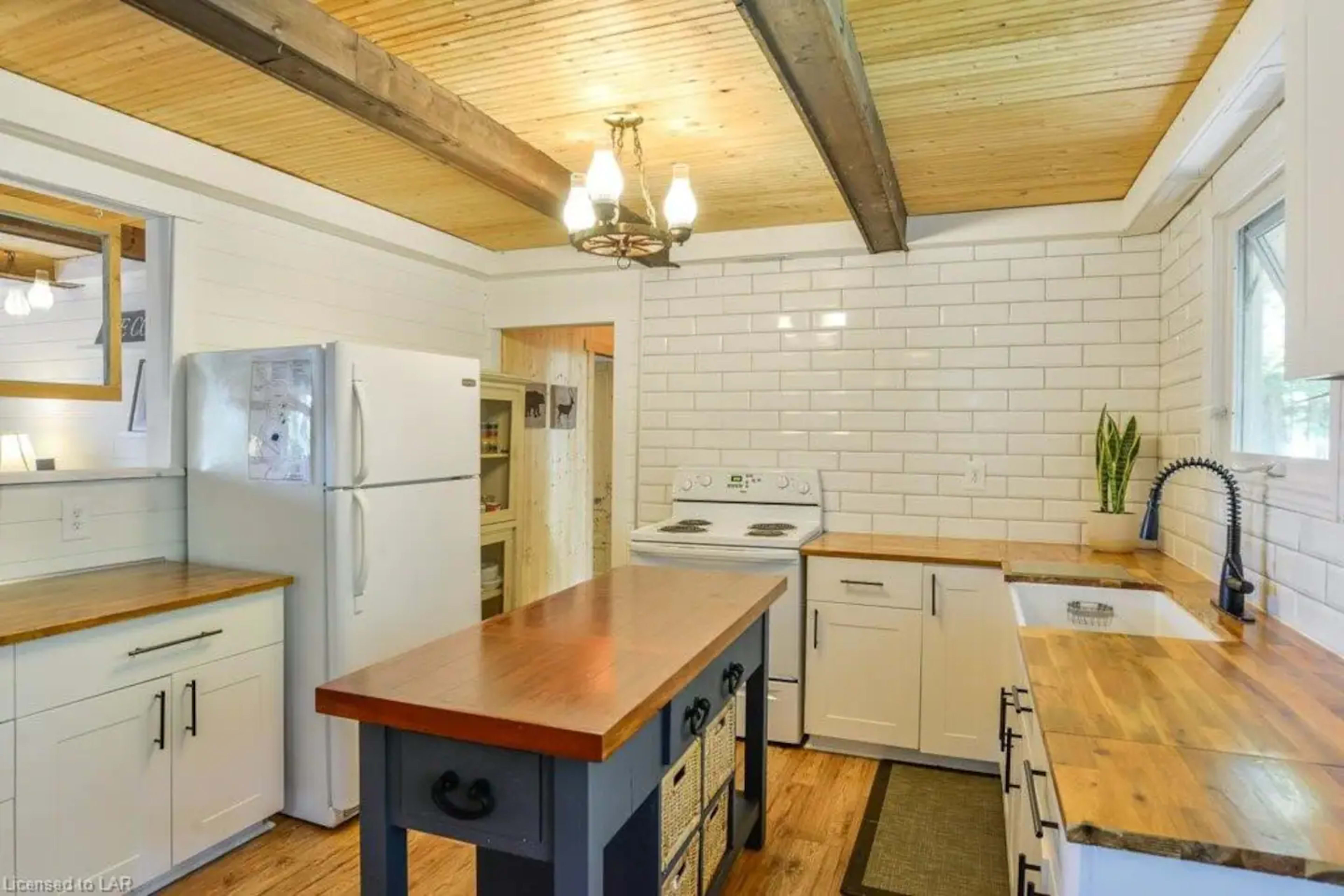 The kitchen features white tiled walls, wooden countertops, and a central island with a dark wood top, complemented by modern appliances and a pendant light fixture.