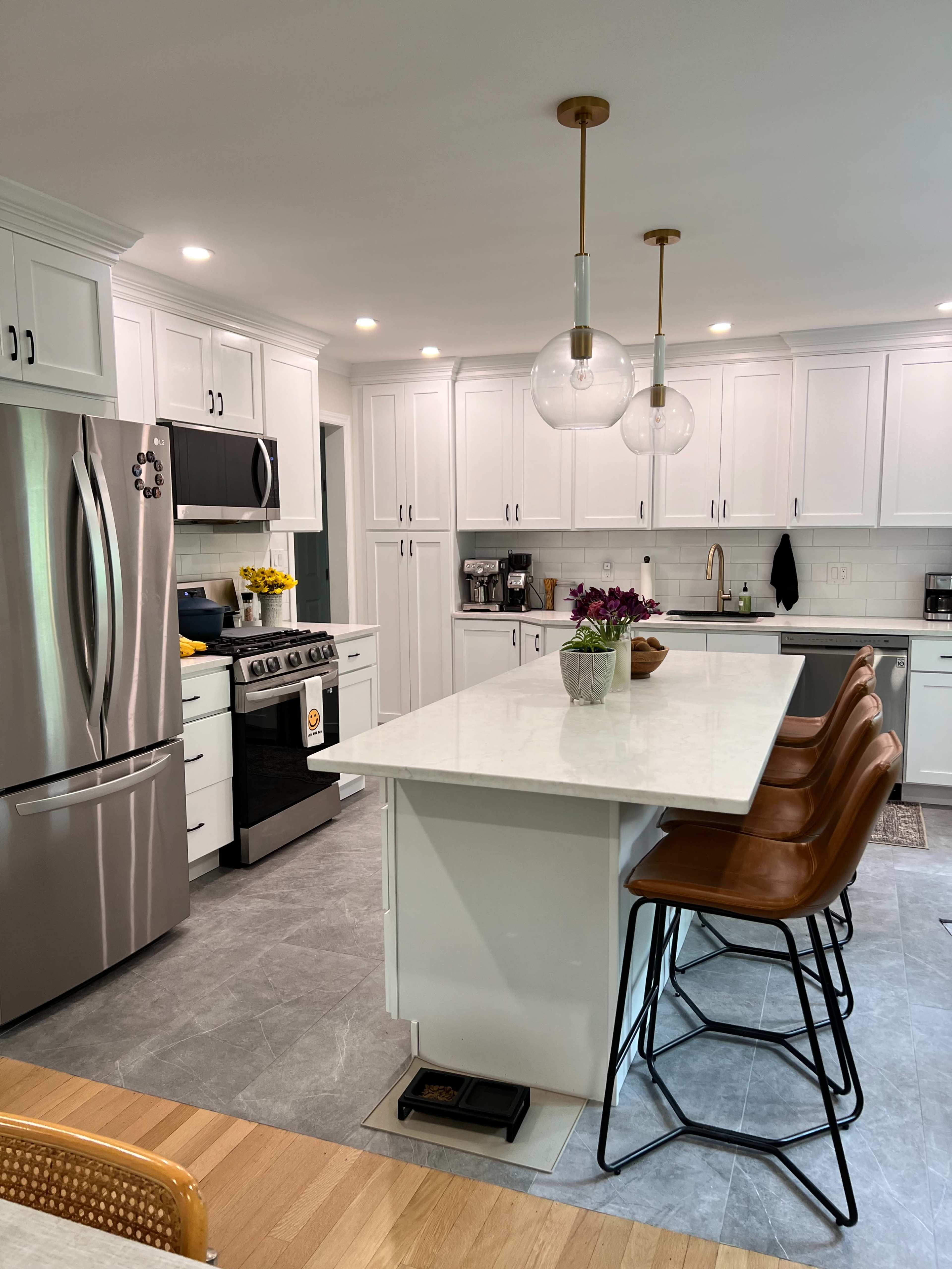 A modern kitchen features white cabinetry, stainless steel appliances, a marble countertop island with bar stools, and pendant lighting.