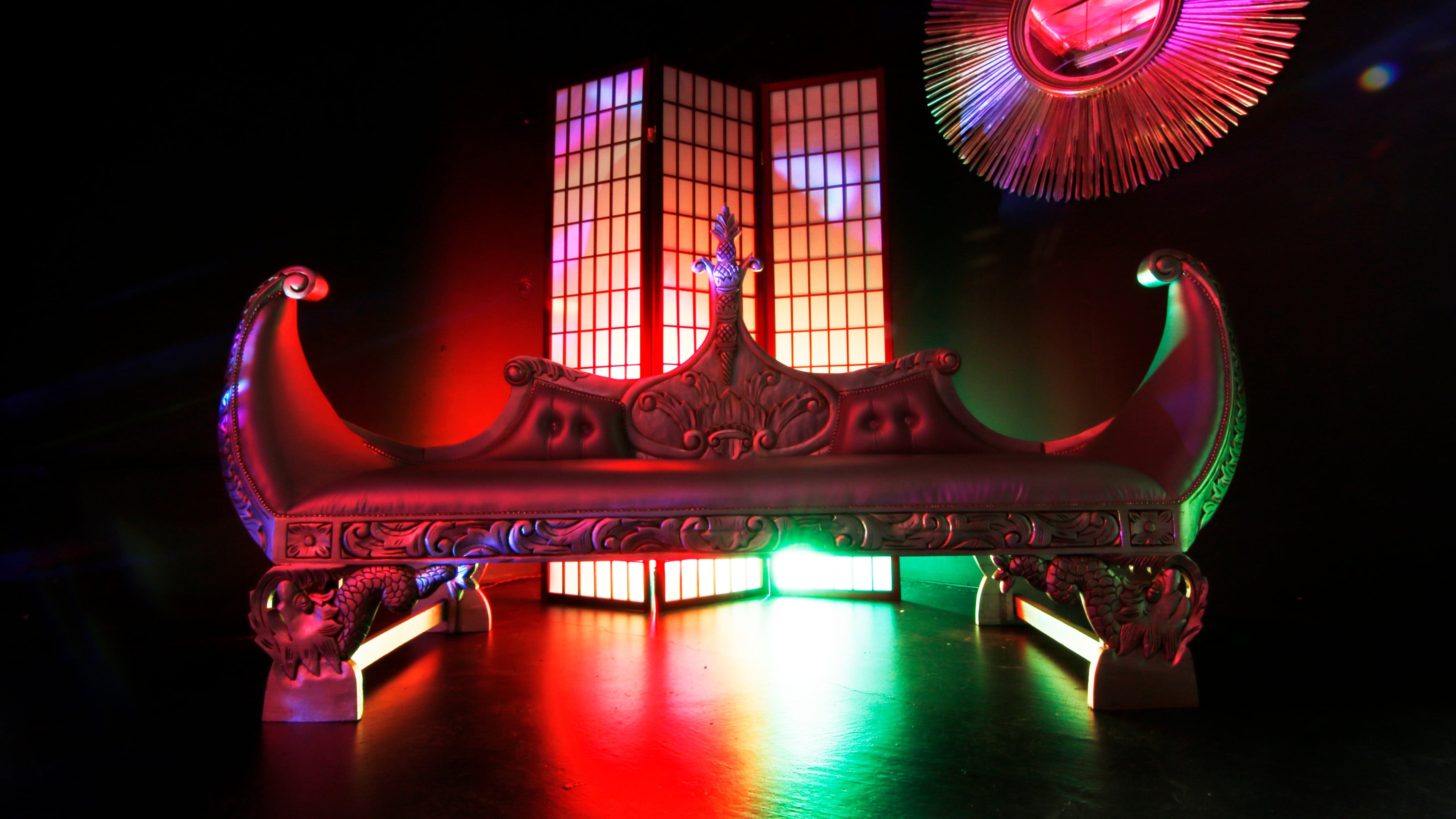 An ornate, curved bench placed in front of a decorative screen, illuminated by colorful lighting.