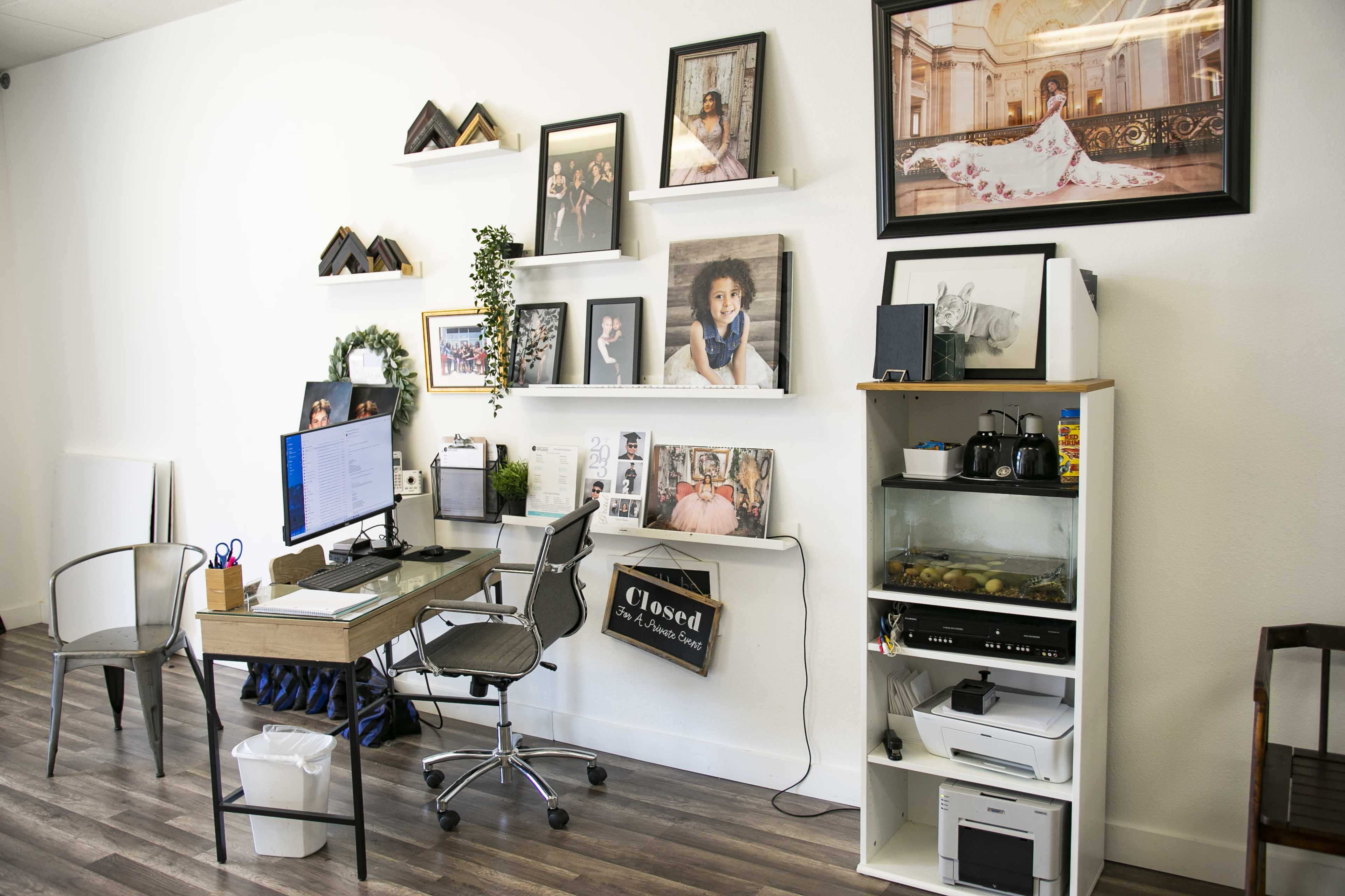 A neatly organized office space featuring a desk with a computer, shelves displaying framed photographs, and a cabinet with a printer and aquarium.