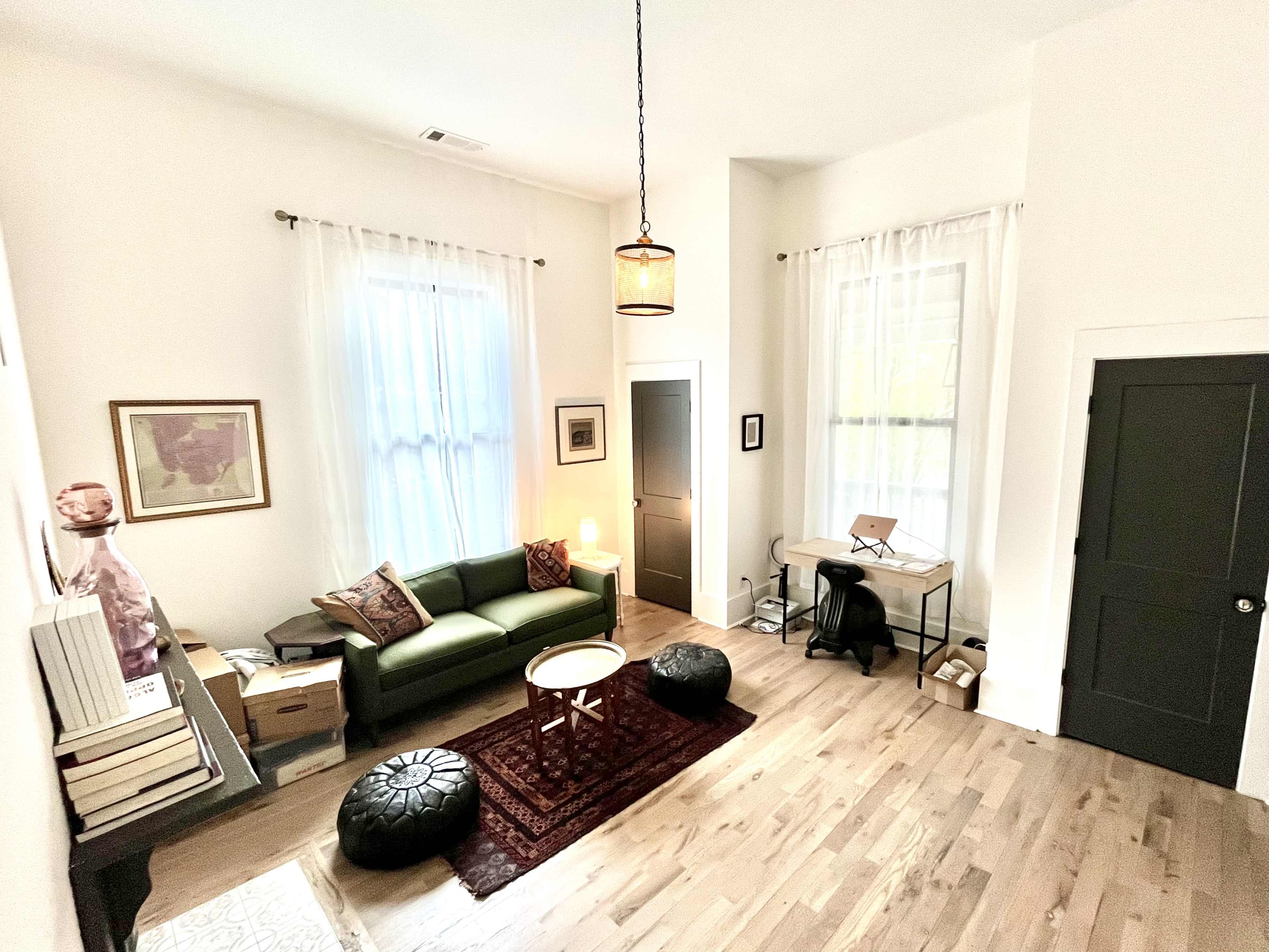 A bright, minimalistic living space with a green sofa, a circular coffee table, and a desk positioned in a corner.